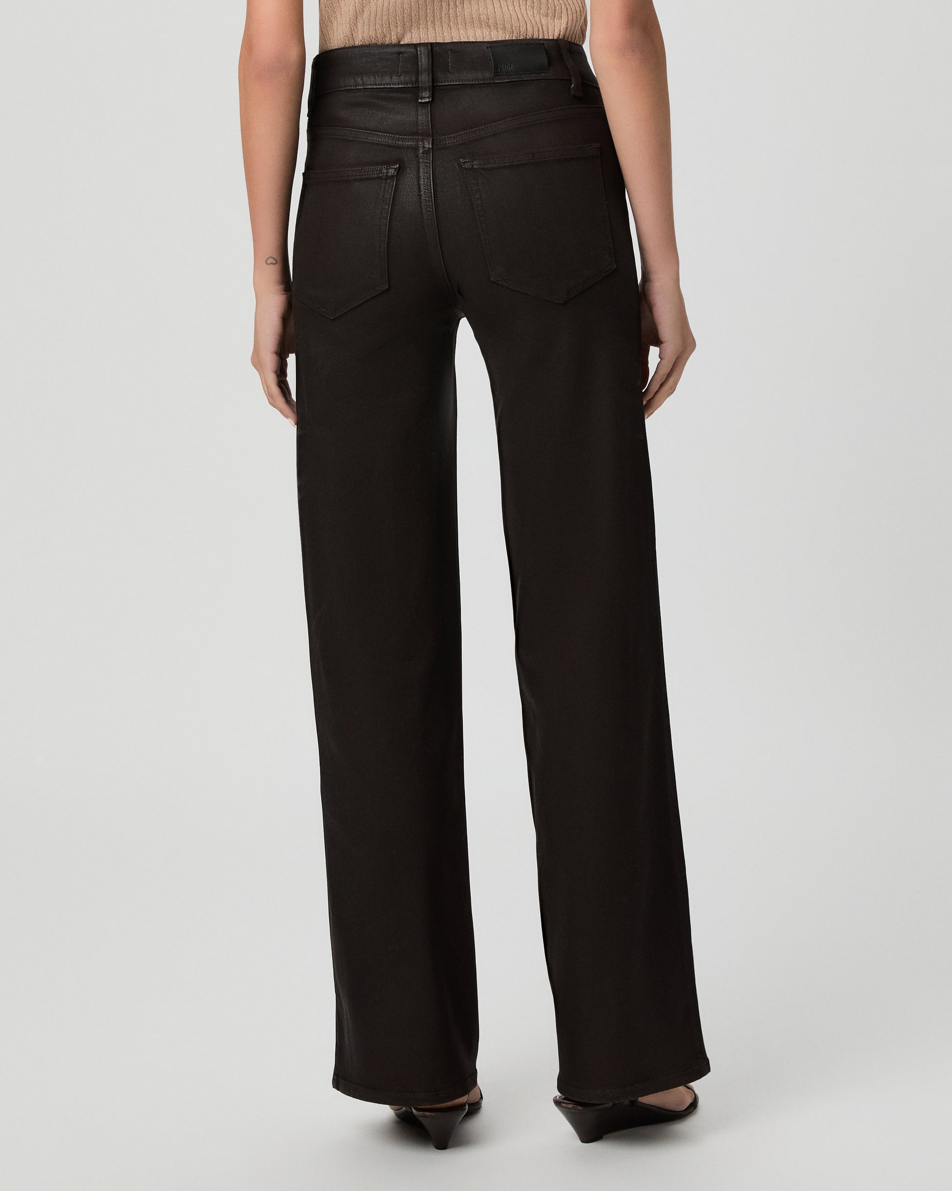 A woman modeling a pair of dark burgundy pants with cream color top and brown sandals against a light gray studio background.