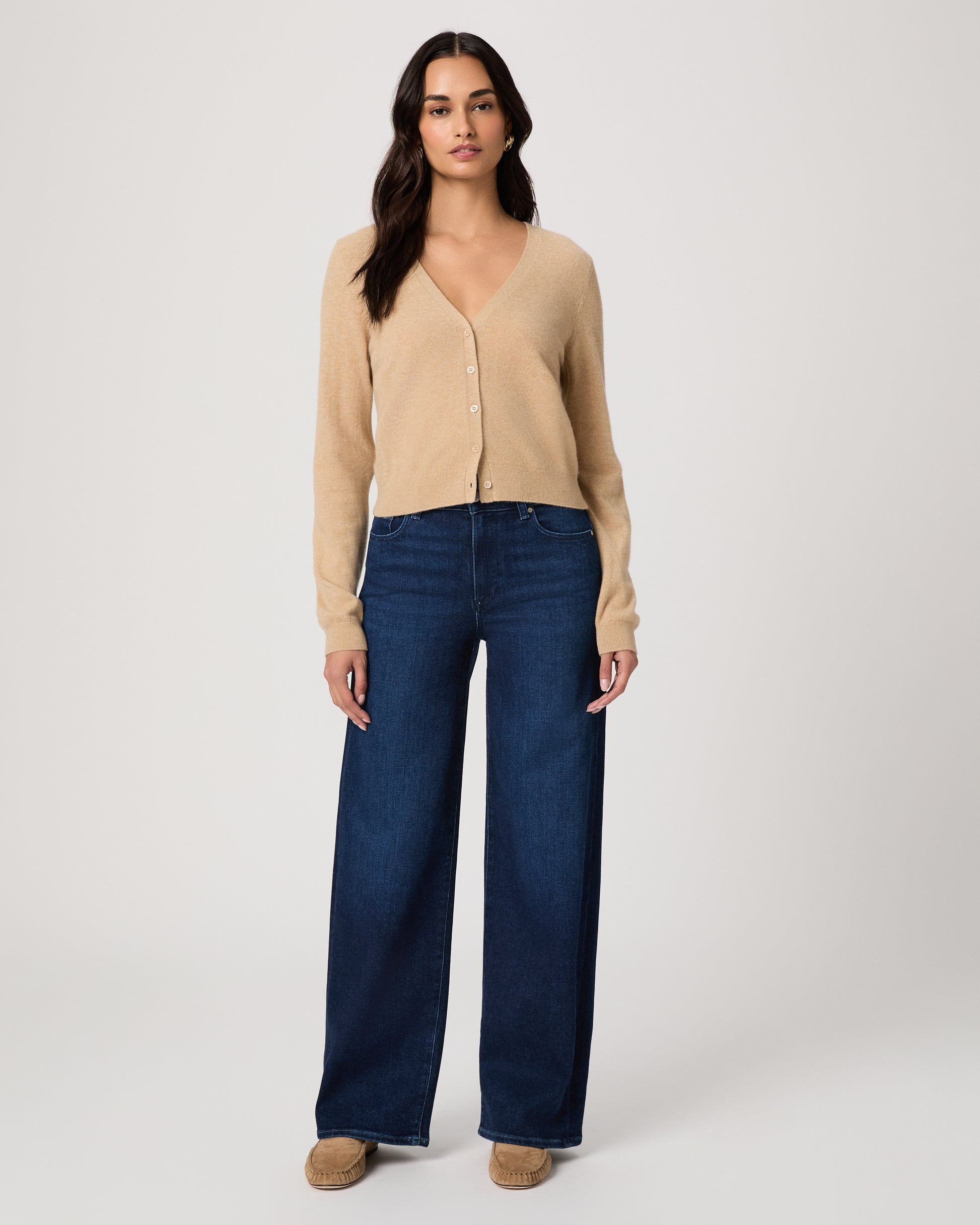 Woman wearing a beige cardigan and blue jeans on a white background