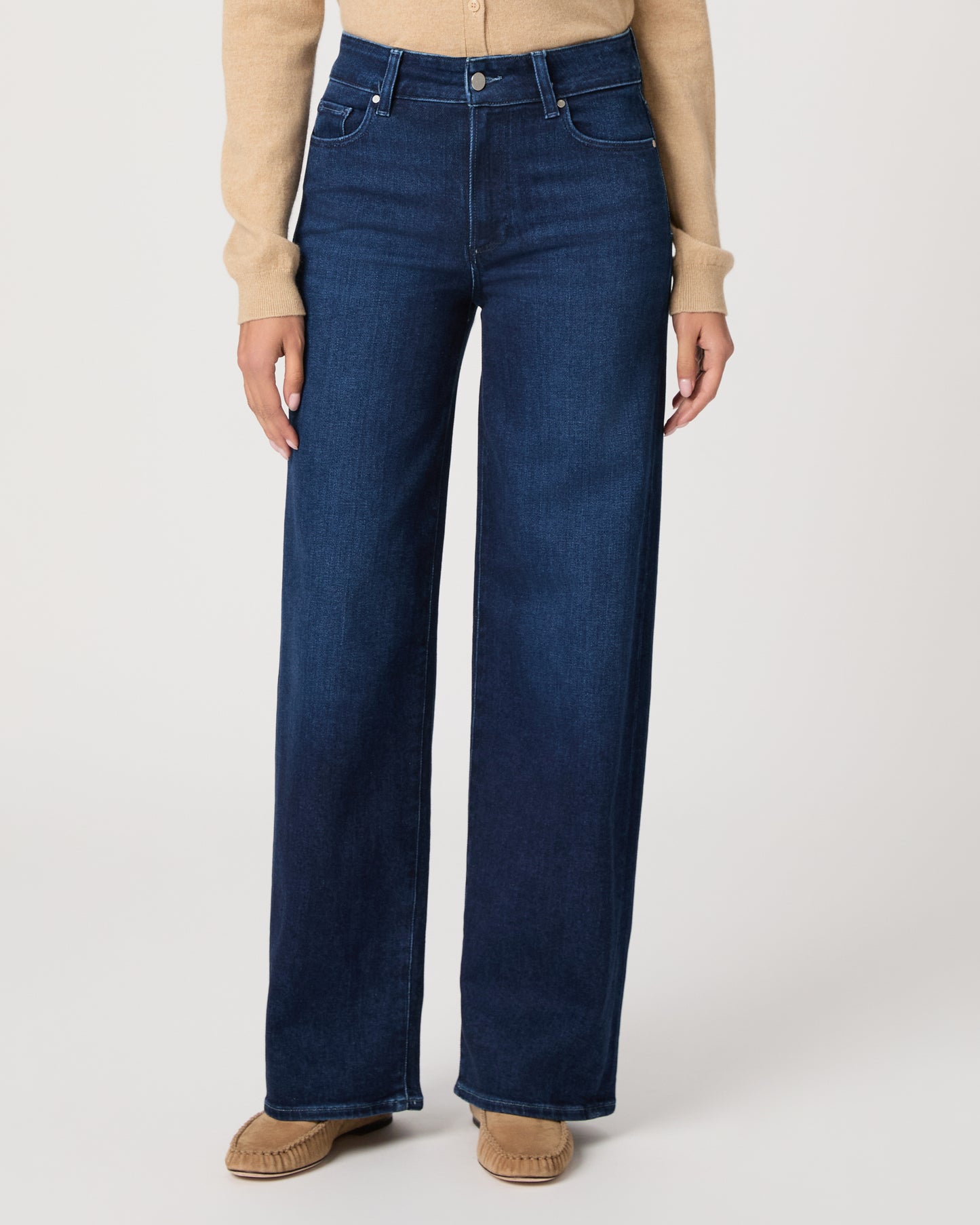 Woman wearing a beige cardigan and blue jeans on a white background