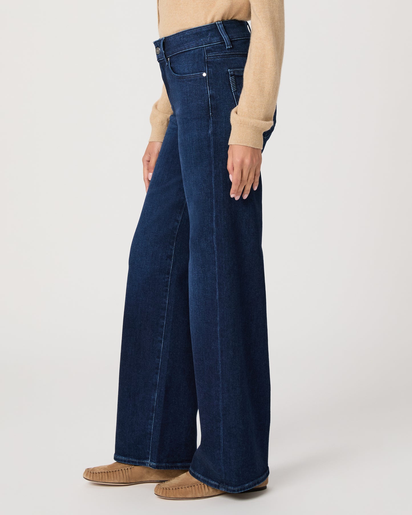 Woman wearing a beige cardigan and blue jeans on a white background
