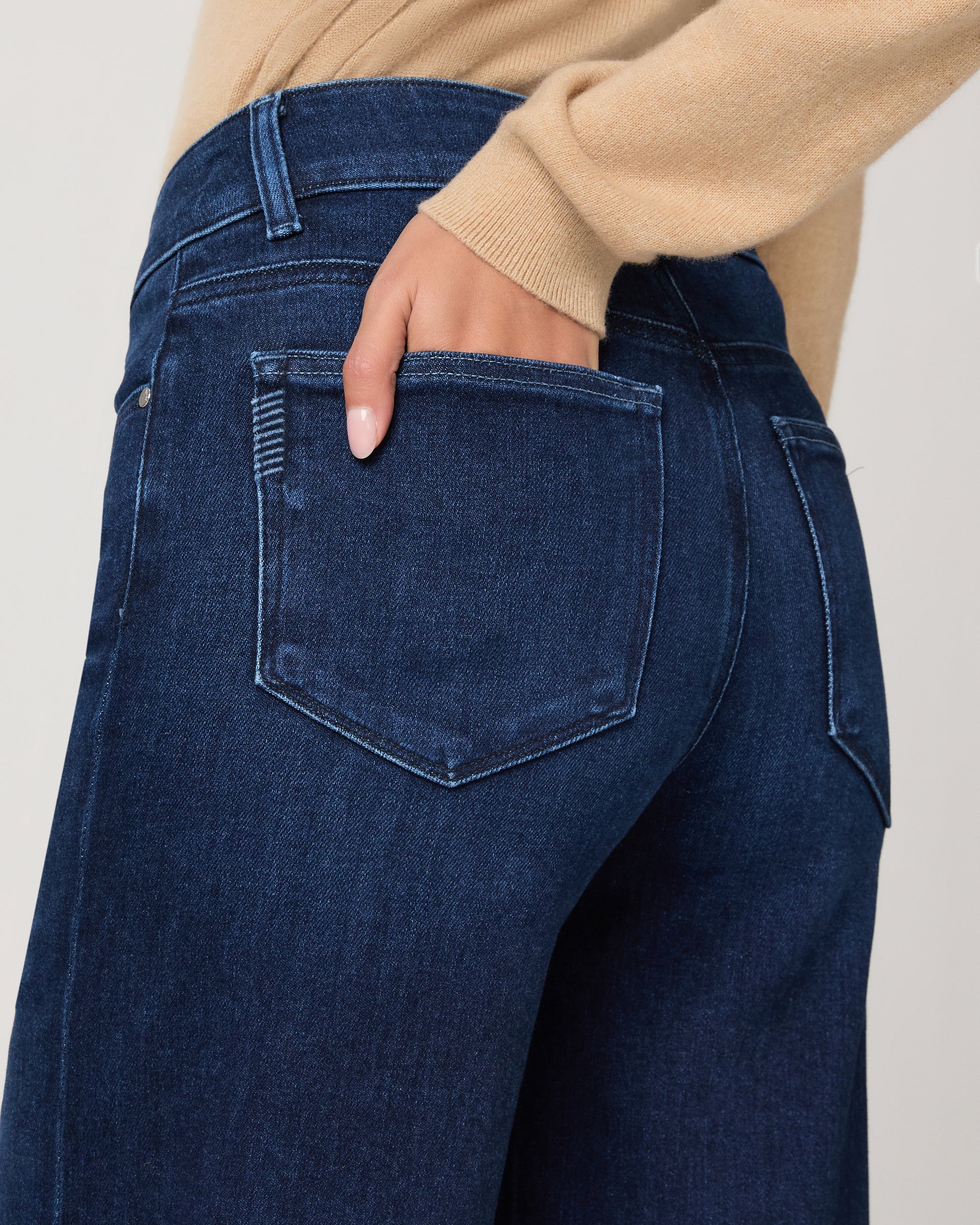 Woman wearing a beige cardigan and blue jeans on a white background