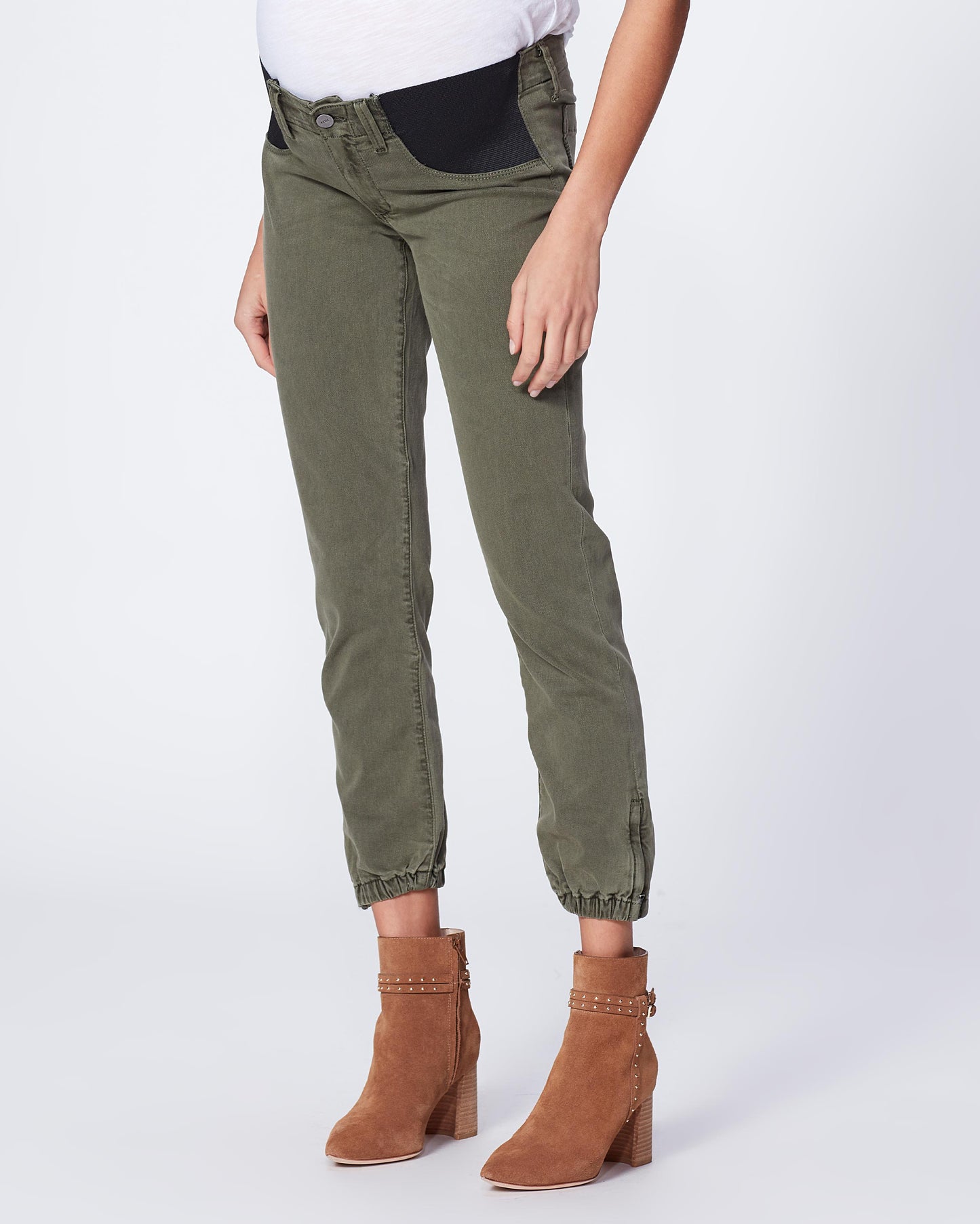 Person wearing olive green pants and brown ankle boots on a white background