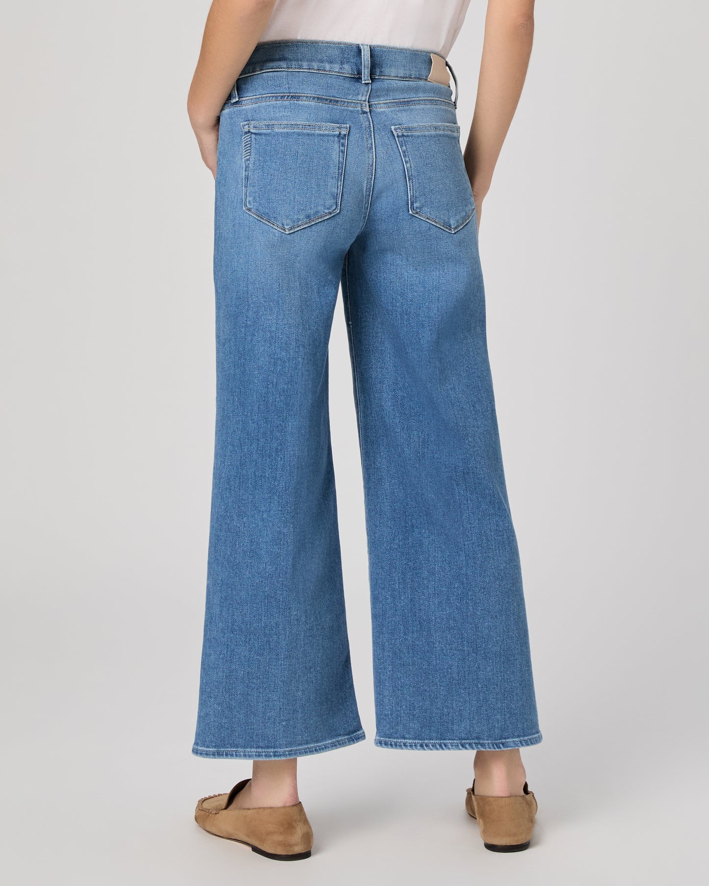 Woman wearing a maternity blue jeans and a white top paired with brown flats on a plain background