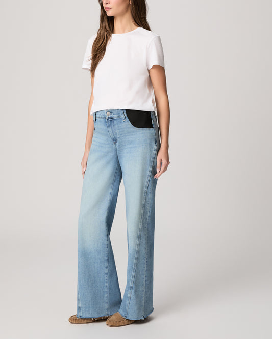 Woman wearing light blue jeans and a white top on a plain background