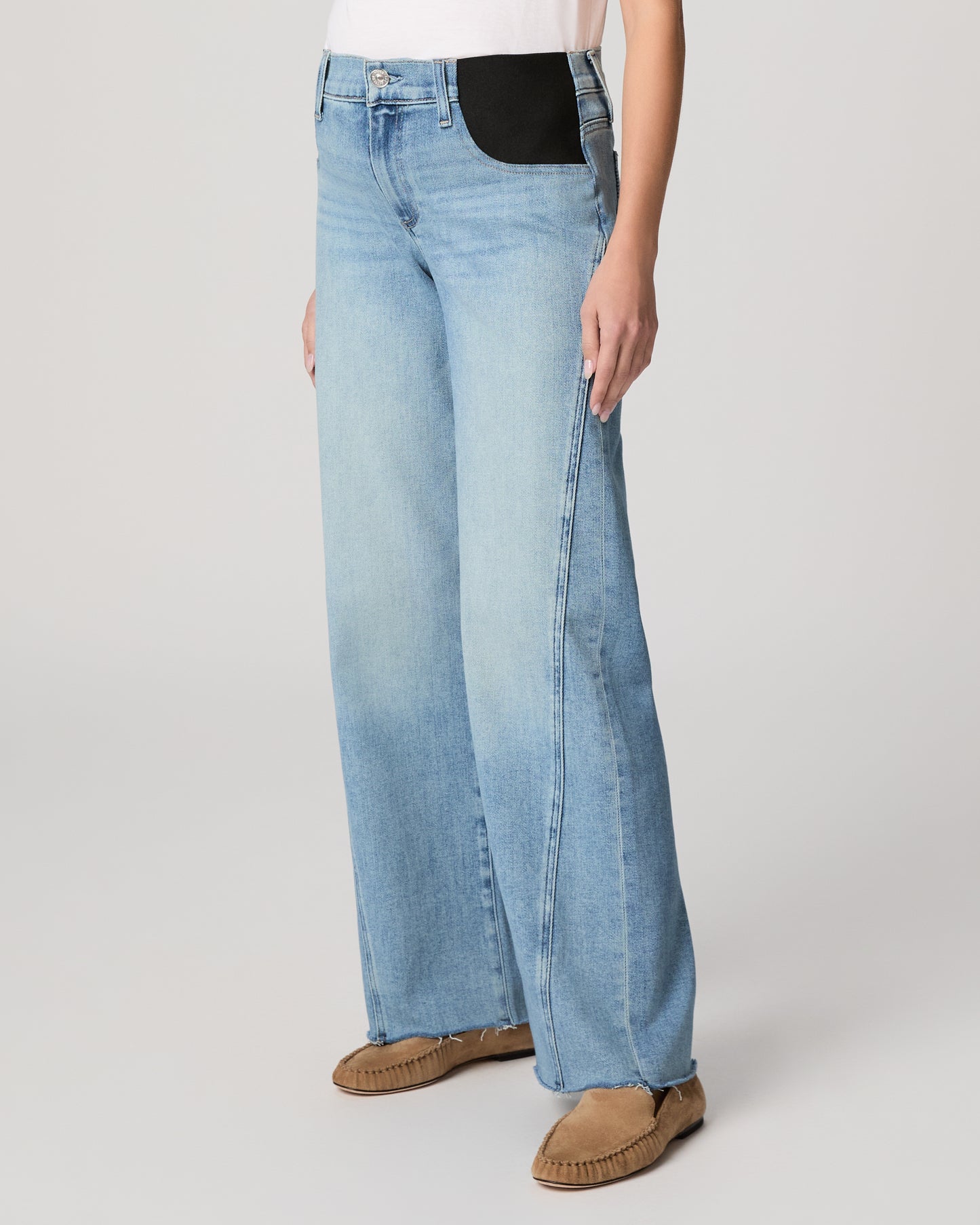 Woman wearing light blue jeans and a white top on a plain background