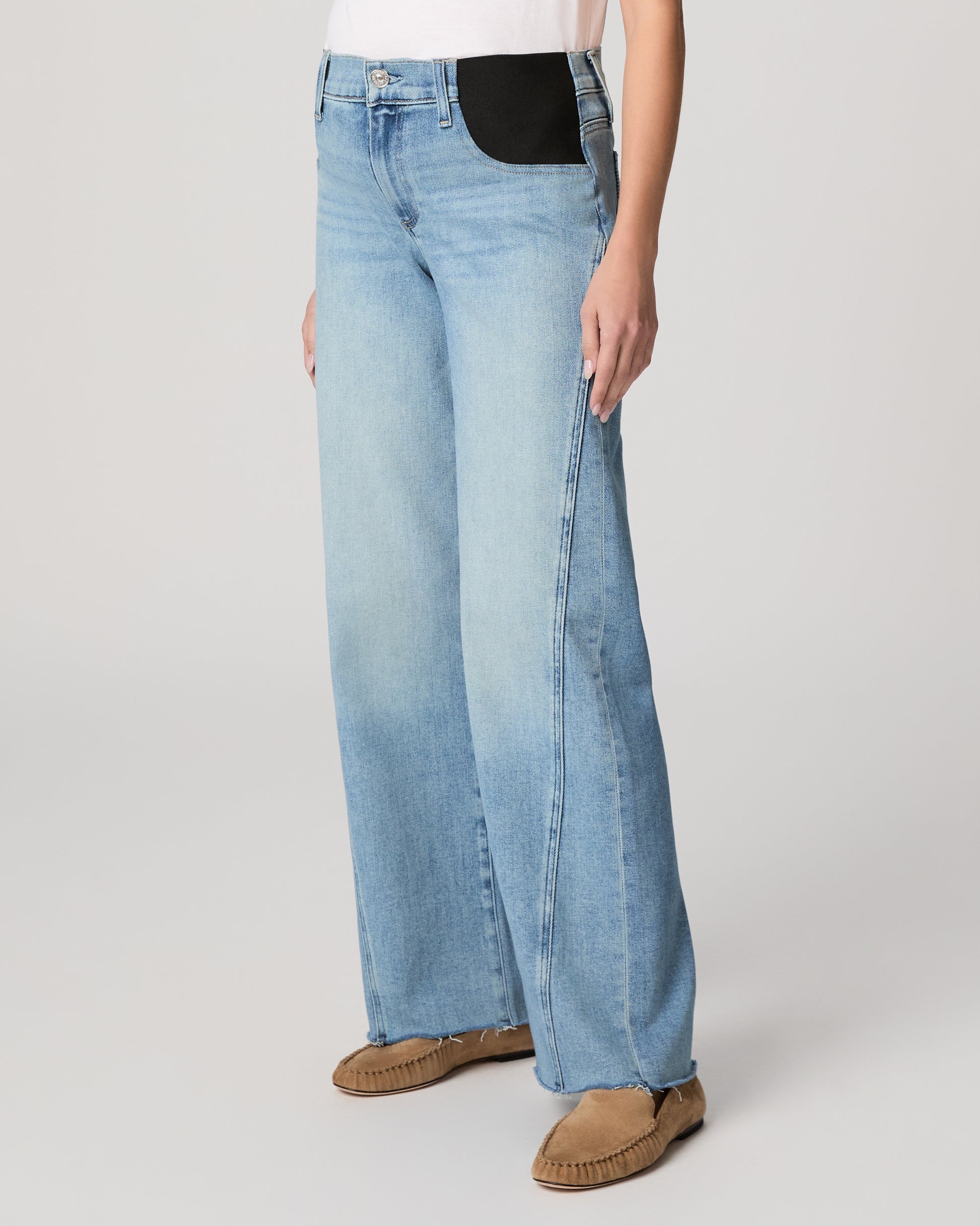 Woman wearing light blue jeans and a white top on a plain background