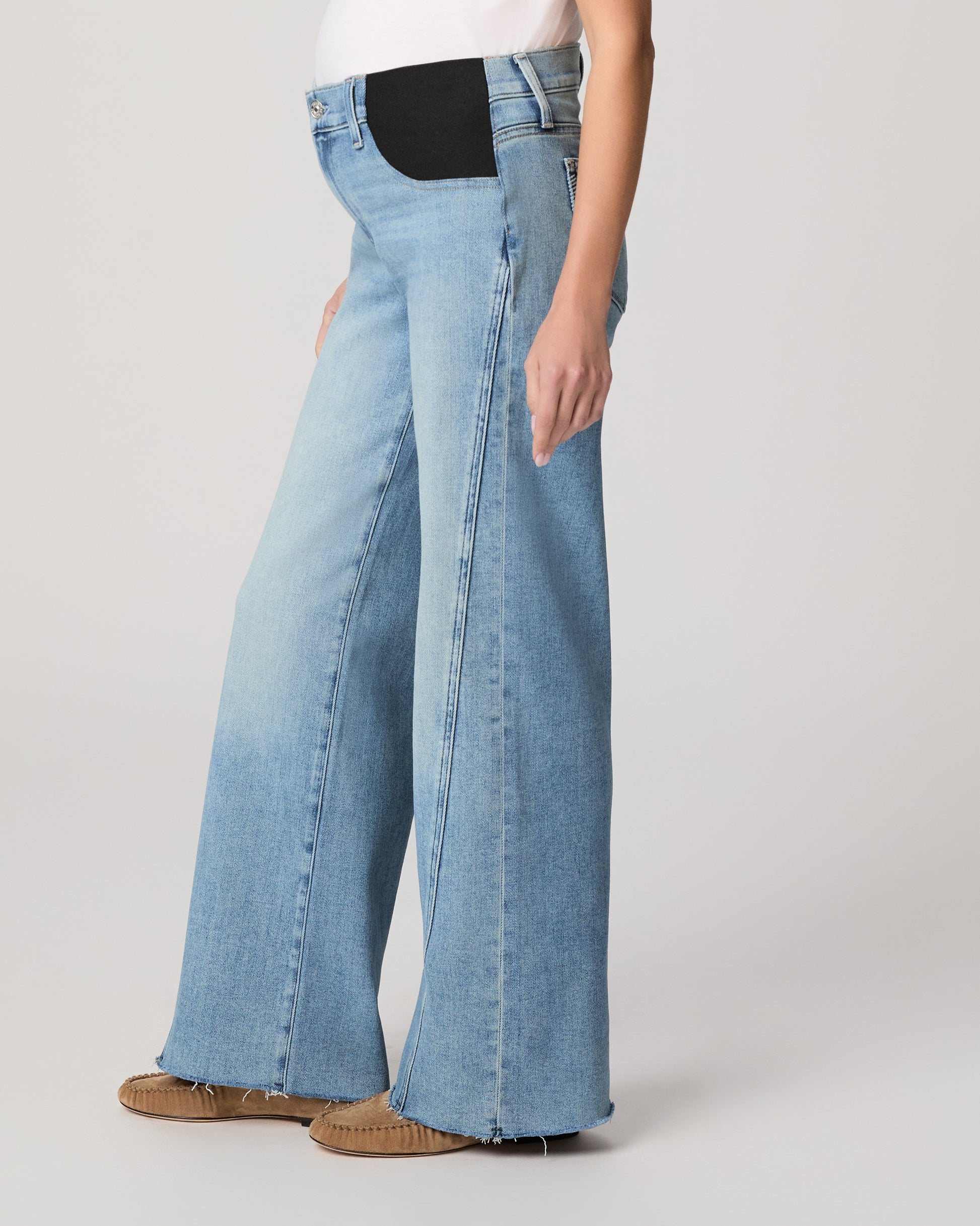 Woman wearing light blue jeans and a white top on a plain background