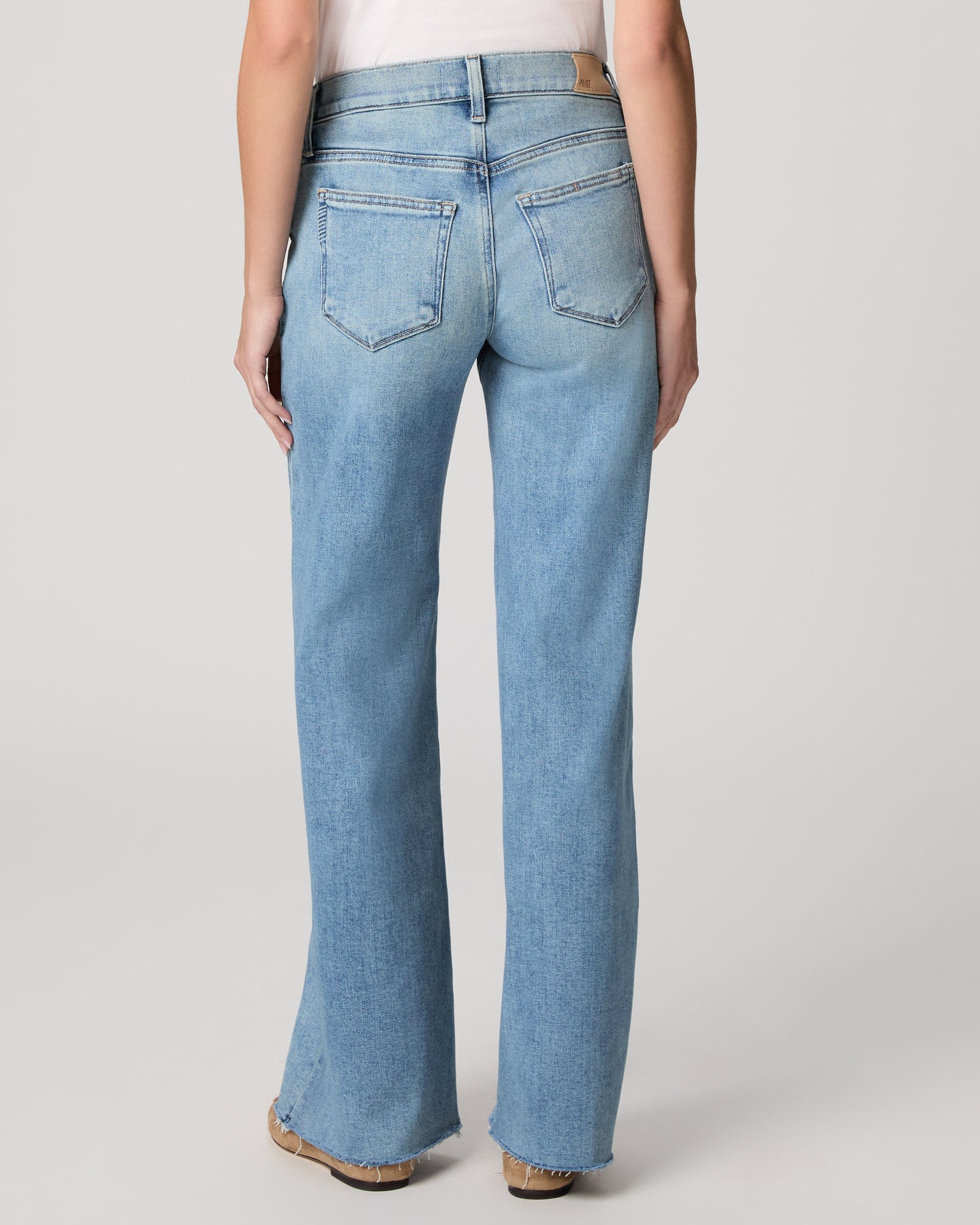 Woman wearing light blue jeans and a white top on a plain background