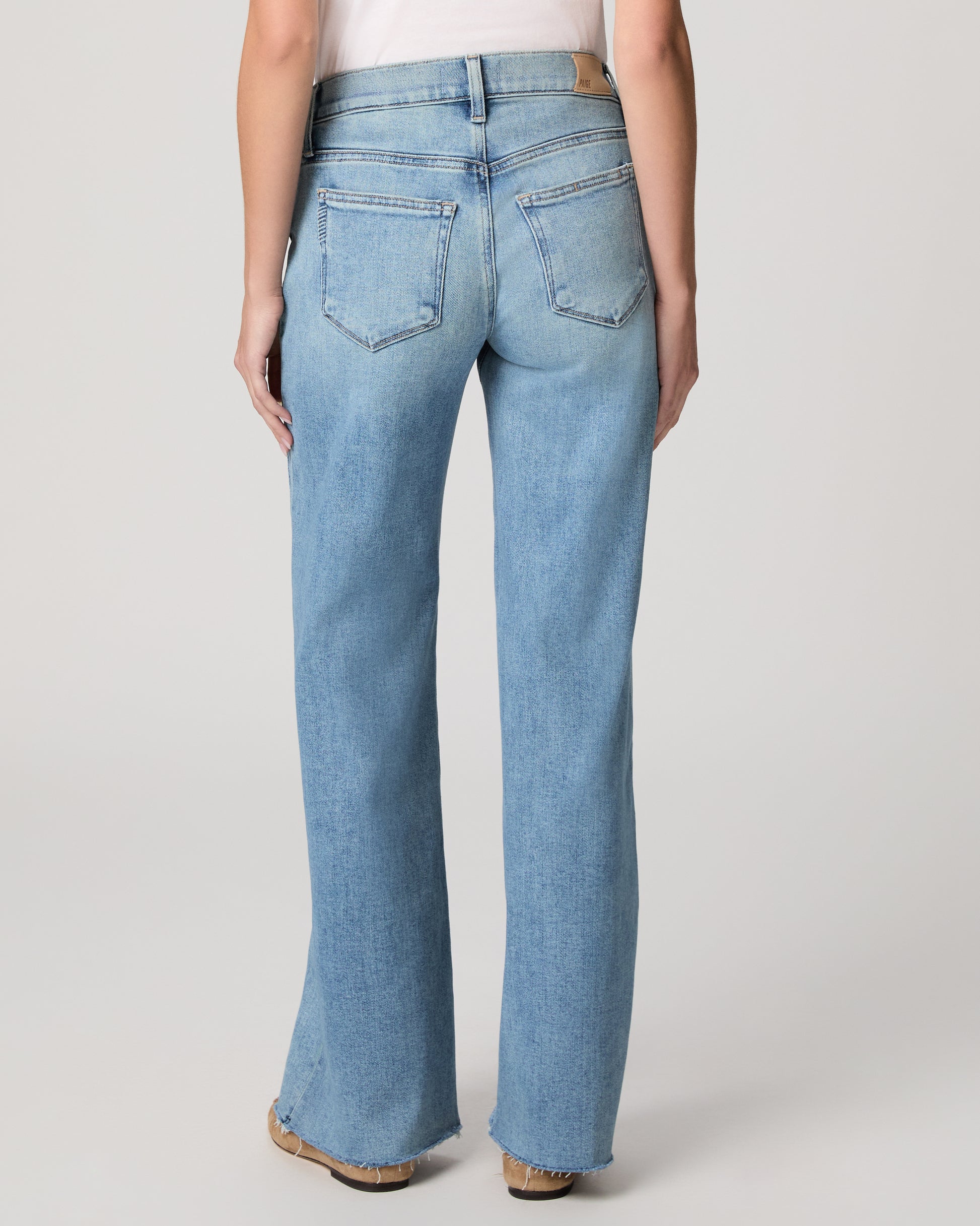 Woman wearing light blue jeans and a white top on a plain background