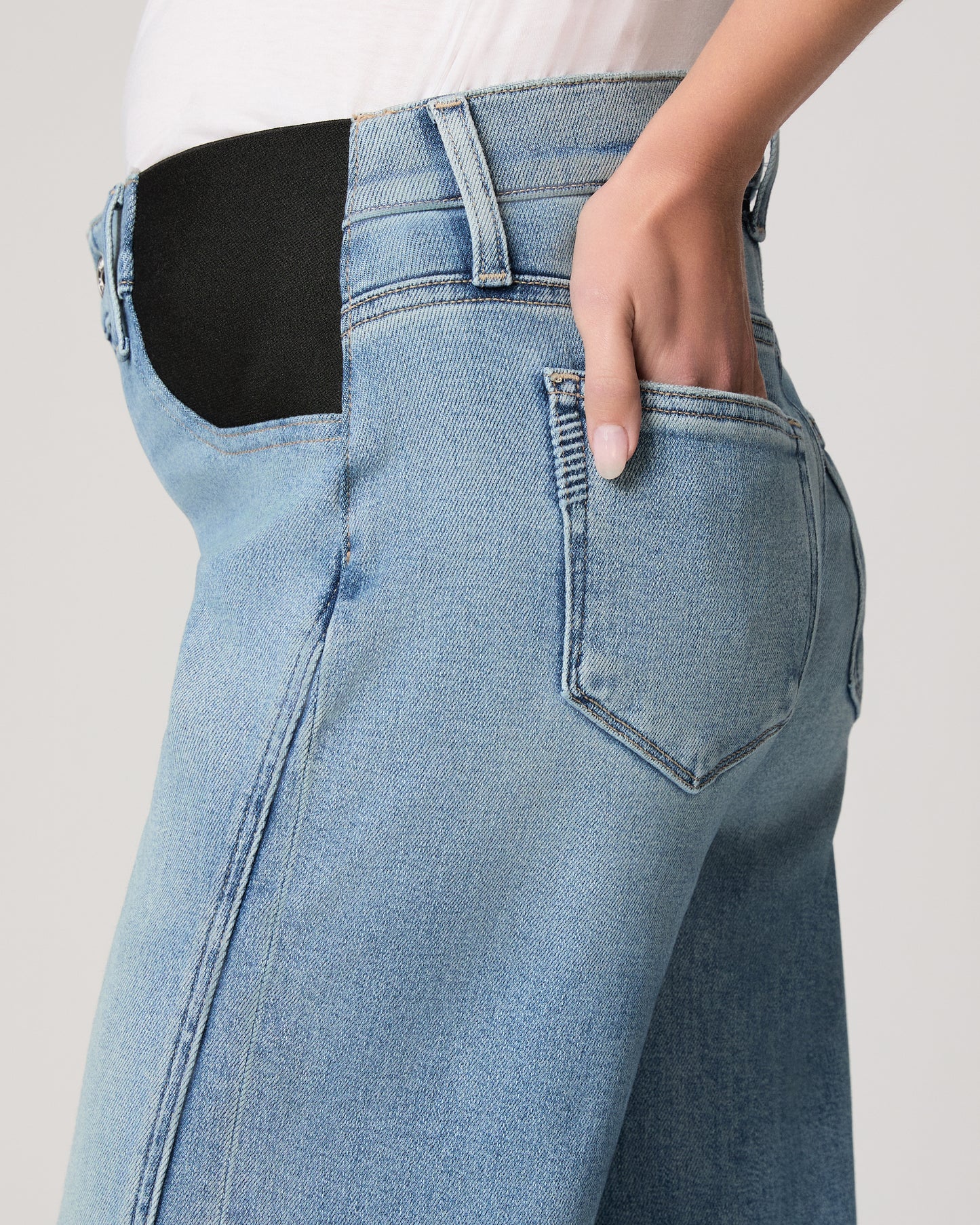 Woman wearing light blue jeans and a white top on a plain background