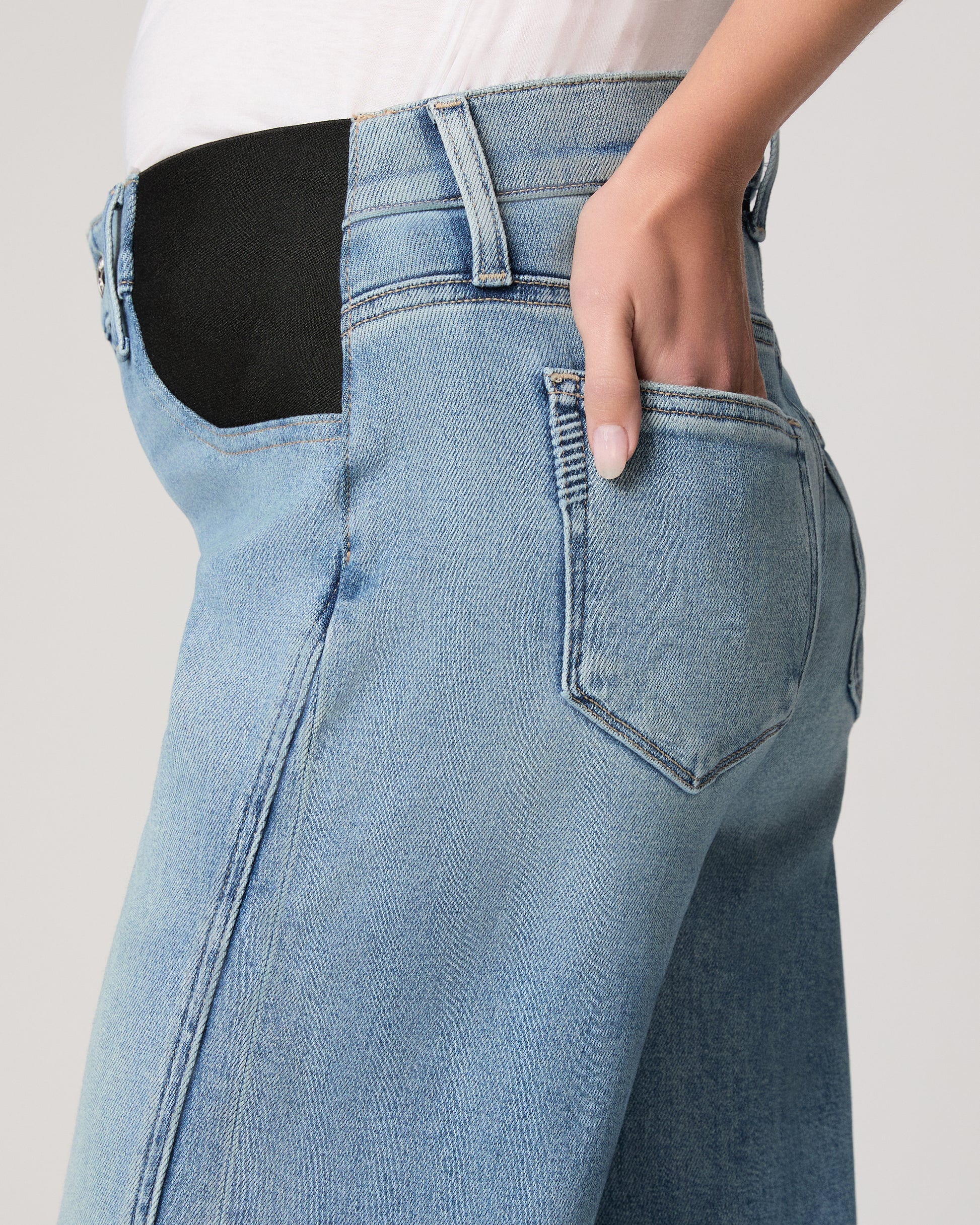 Woman wearing light blue jeans and a white top on a plain background