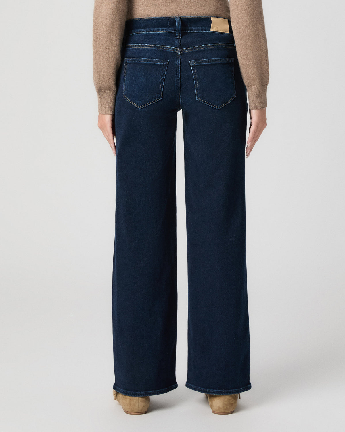 Back view from the waist down of model in a camel sweater, showing the back pockets and wide leg of Anessa Maternity Jeans in Amagansett with tan flats