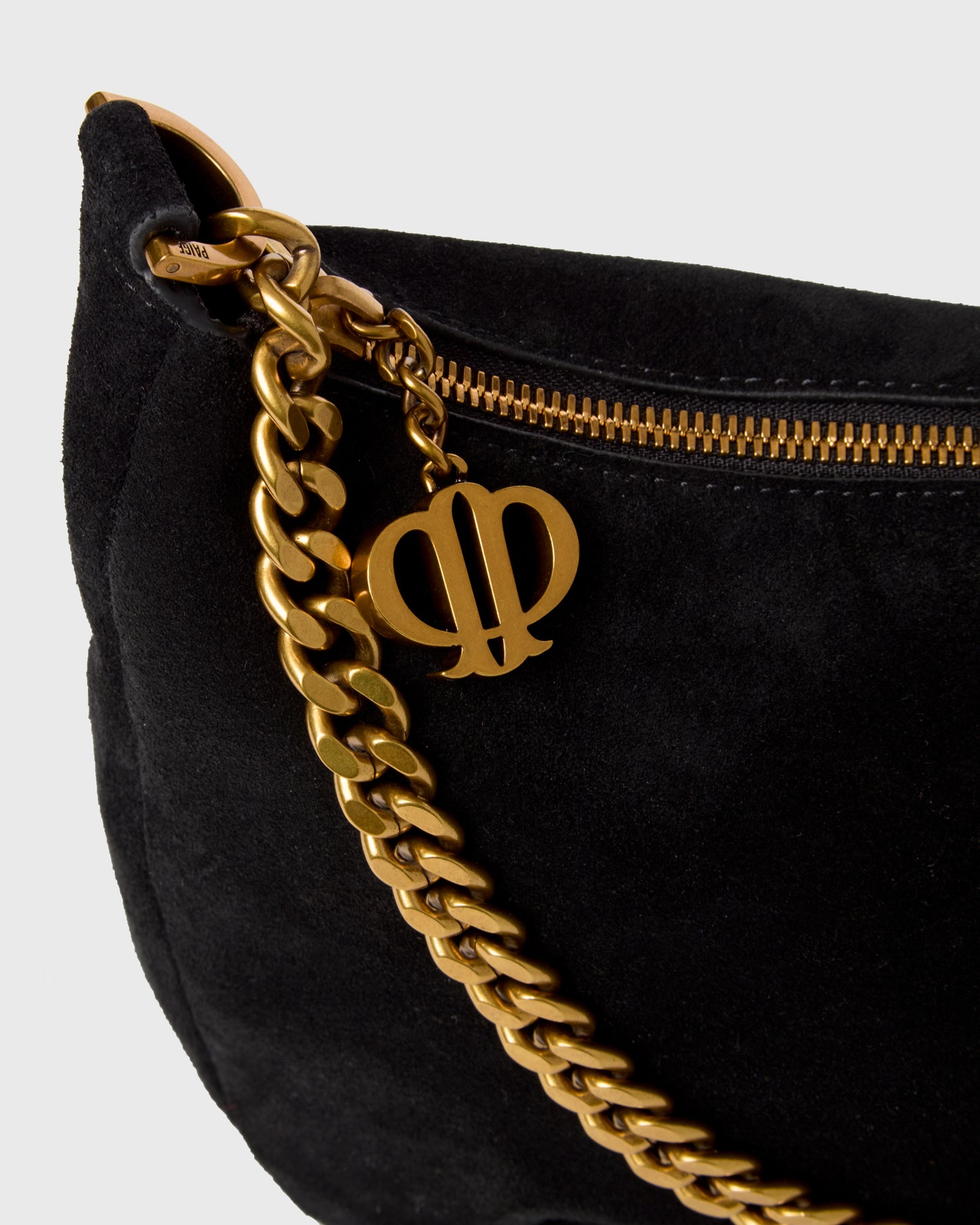 Close-up of a black suede shoulder bag with a chunky gold chain strap and a gold double-phi emblem charm, set against a light gray background.
