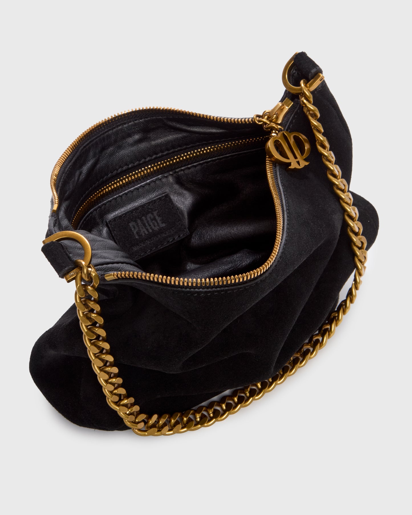 A black suede crescent-shaped shoulder bag with a gold-tone chain strap and a small gold logo charm, set against a plain light gray background.