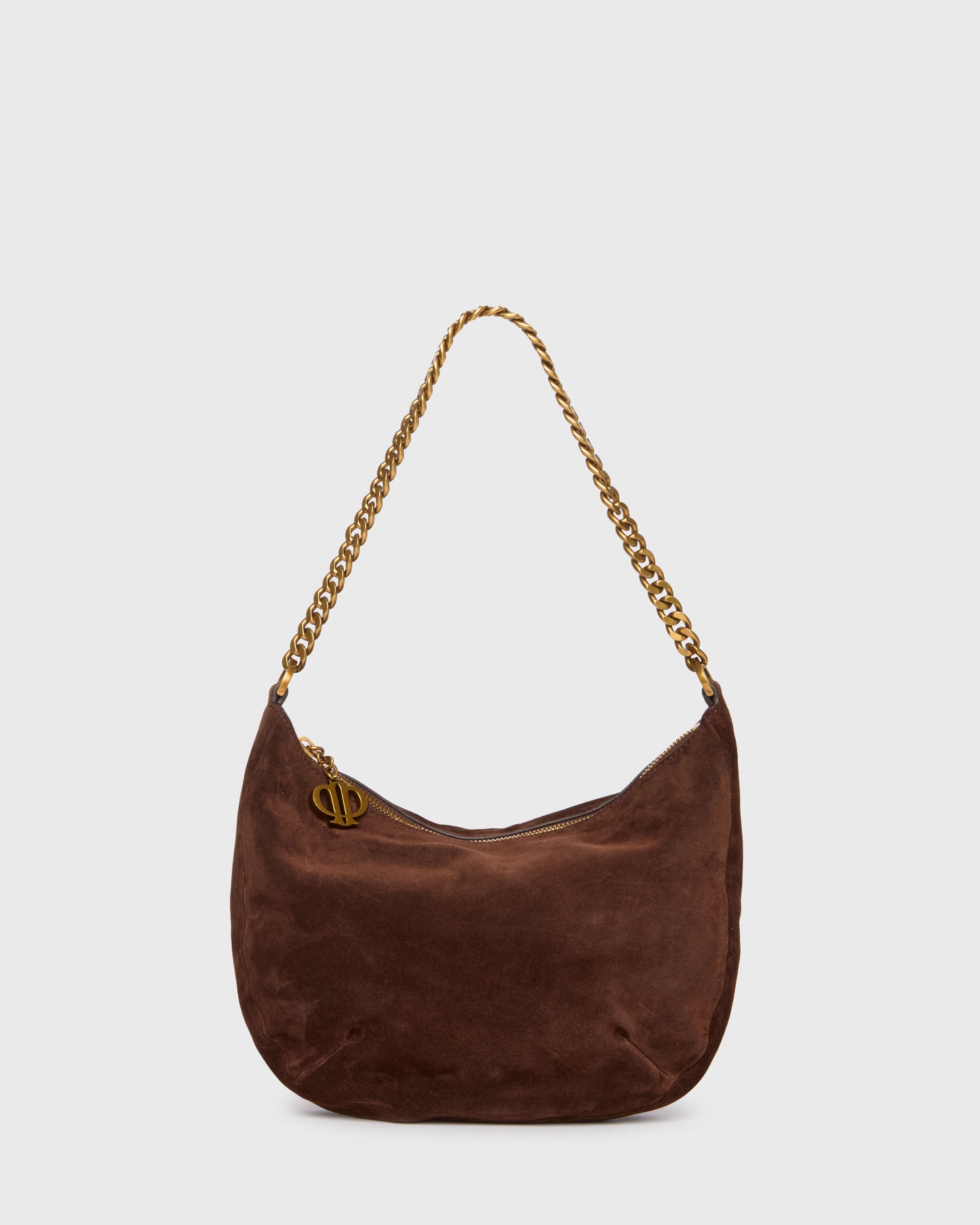 A dark brown suede crescent shoulder bag with a gold-tone chain strap and a small gold-tone metal logo charm, shown against a light gray background.