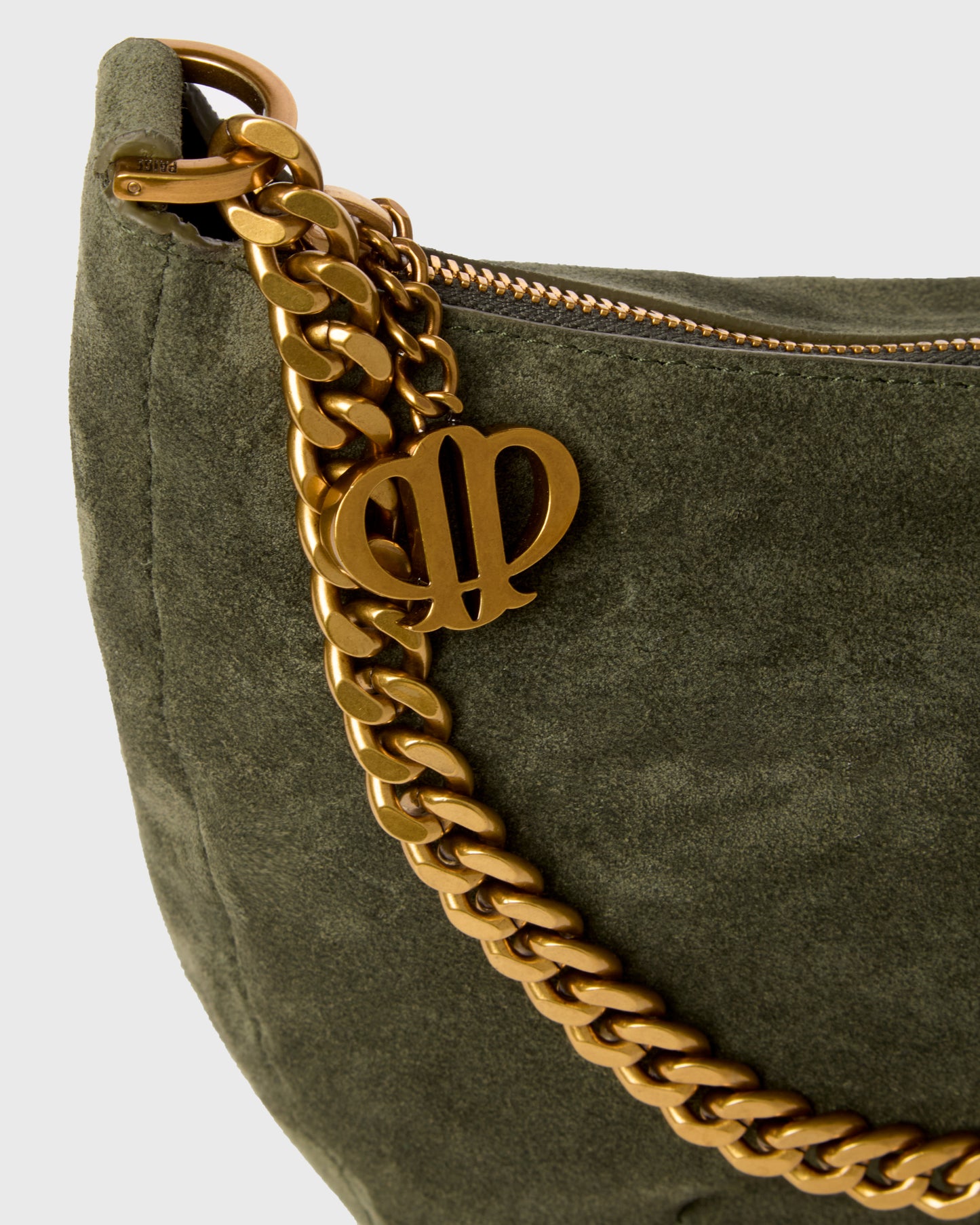 Close-up of an olive green suede shoulder bag with a chunky gold chain strap and a gold interlocking 'DP' logo charm, set against a light gray background.
