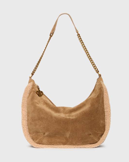 A tan suede crescent-shaped shoulder bag with a beige textured trim and a gold-tone chain strap, shown against a light gray background.