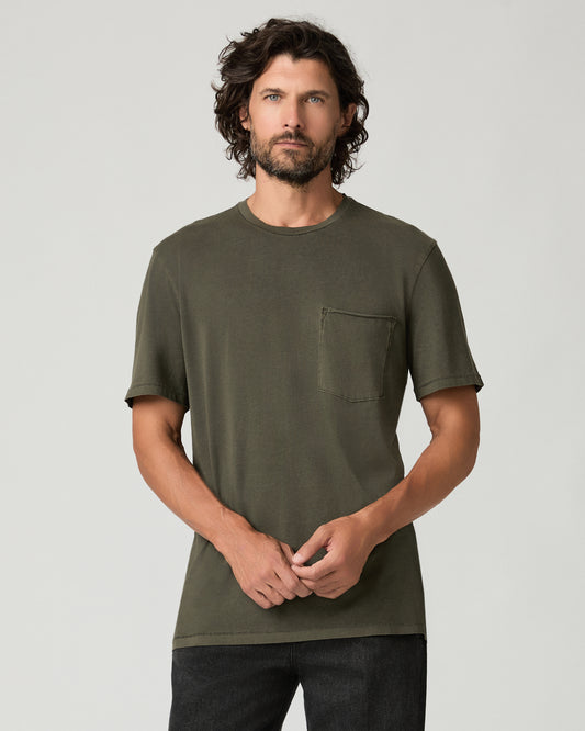 Cropped front view of a man with curly hair clasping his hands in front of him, wearing a vintage fatigue green crew-neck tee with a raw-edge chest pocket and short sleeves.