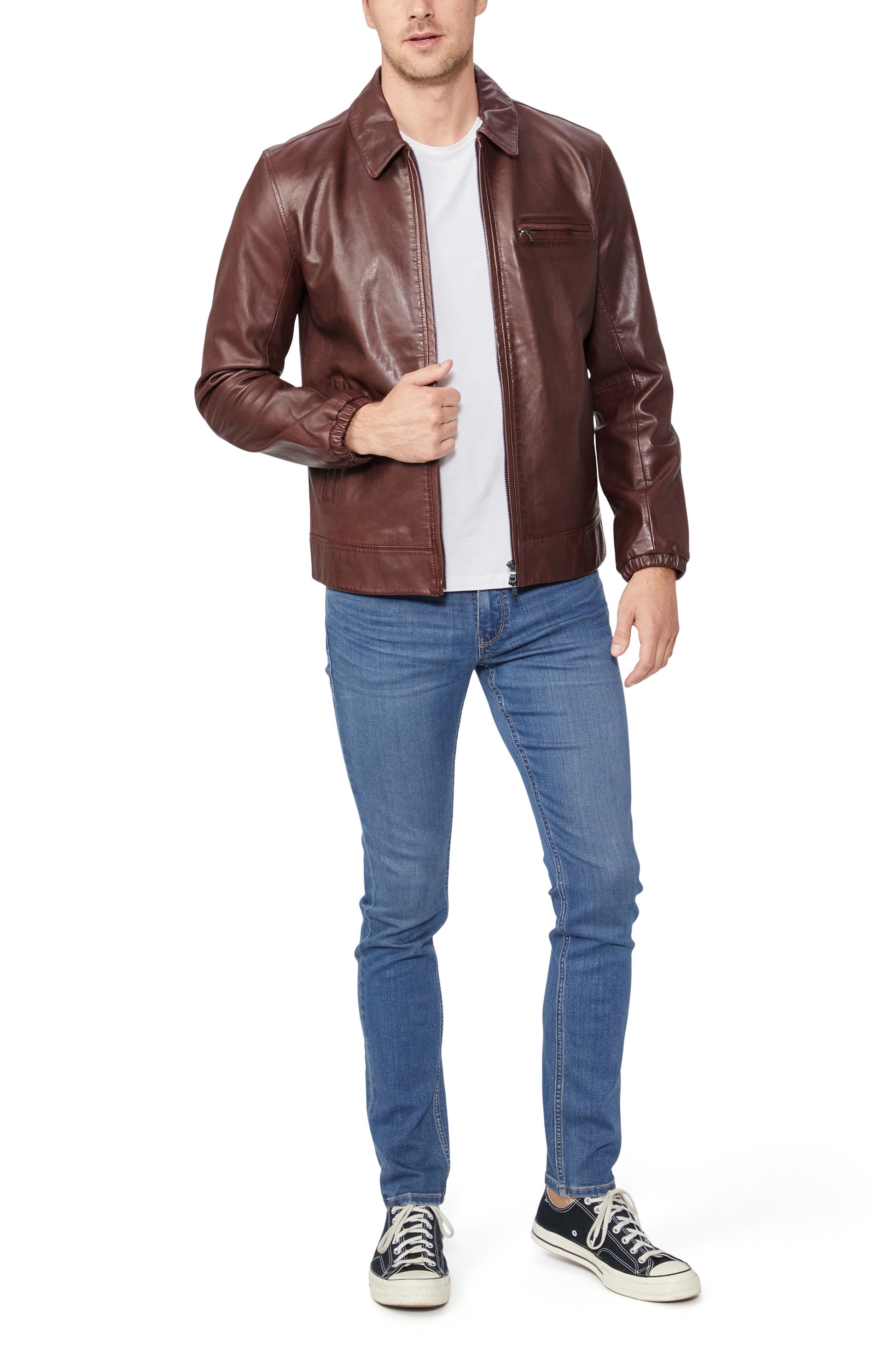 Man wearing a brown leather jacket, white shirt, blue jeans, and black sneakers on a white background