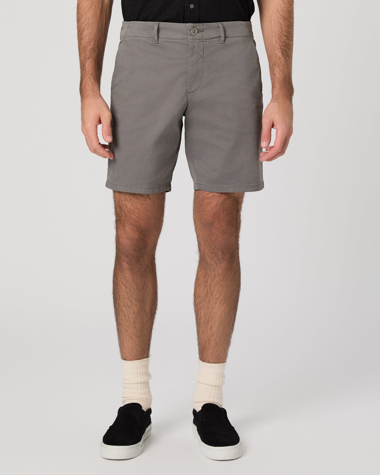 Man wearing black short sleeve shirt paired with grey shorts and black sneakers against a white background