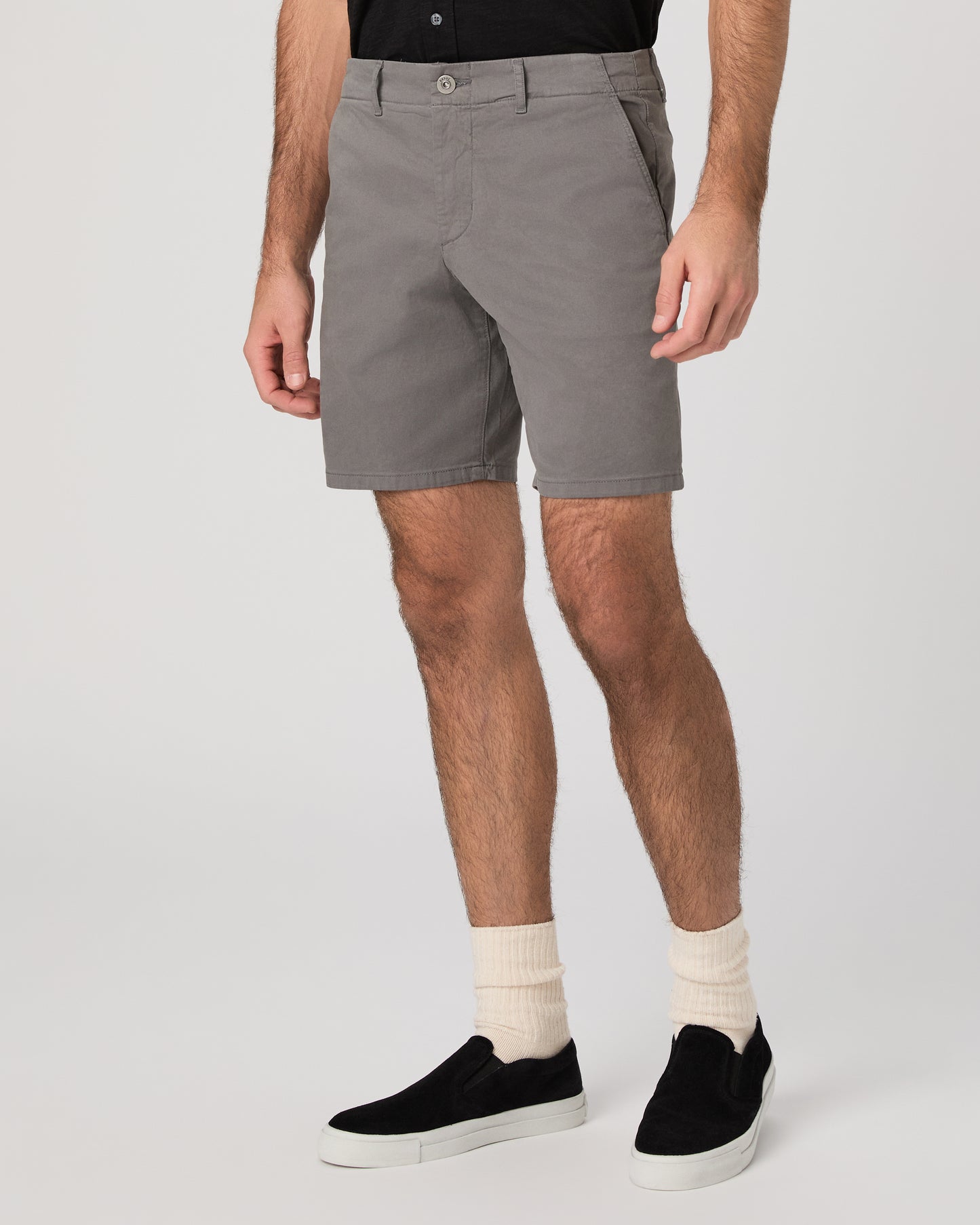 Man wearing black short sleeve shirt paired with grey shorts and black sneakers against a white background