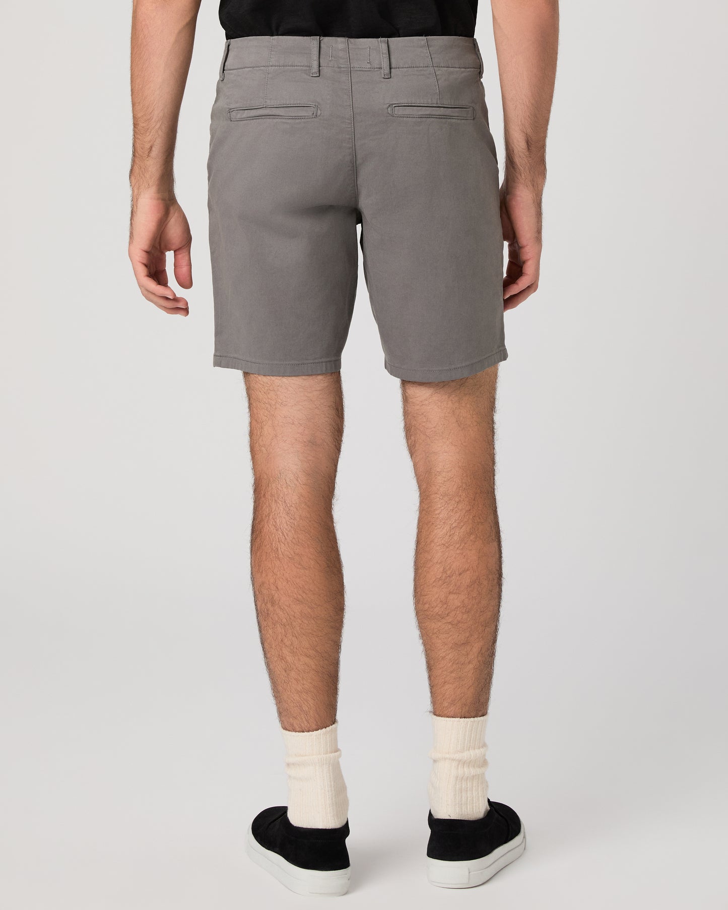 Man wearing black short sleeve shirt paired with grey shorts and black sneakers against a white background
