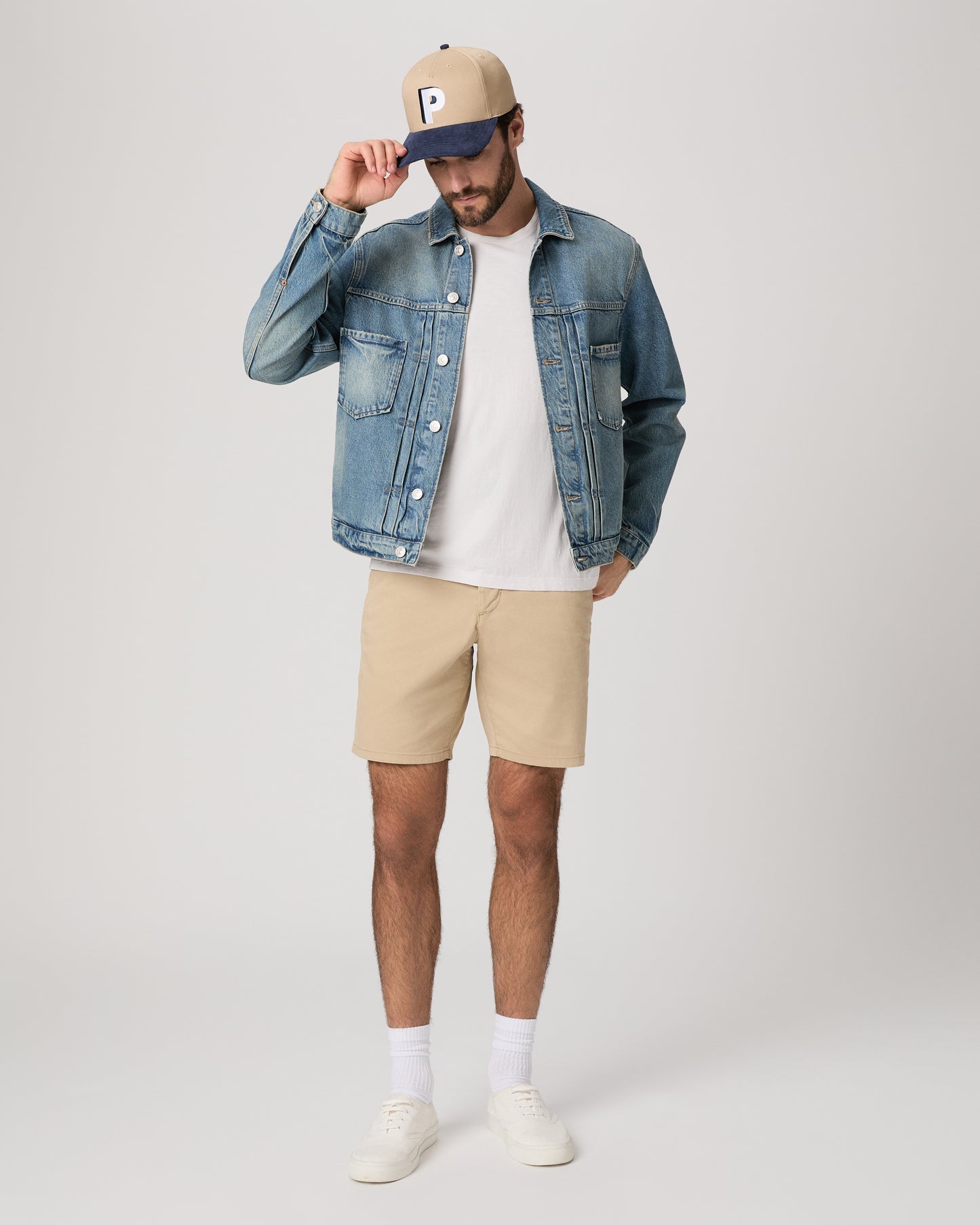 Men wearing a denim jacket, white tee, beige color shorts paired with a baseball cap and white sneakers