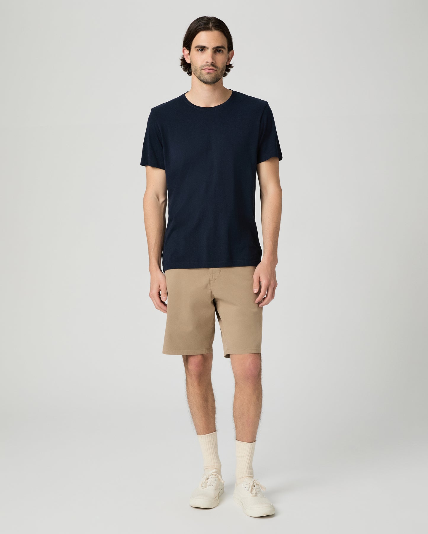 Man wearing a navy t-shirt and beige shorts on a white background