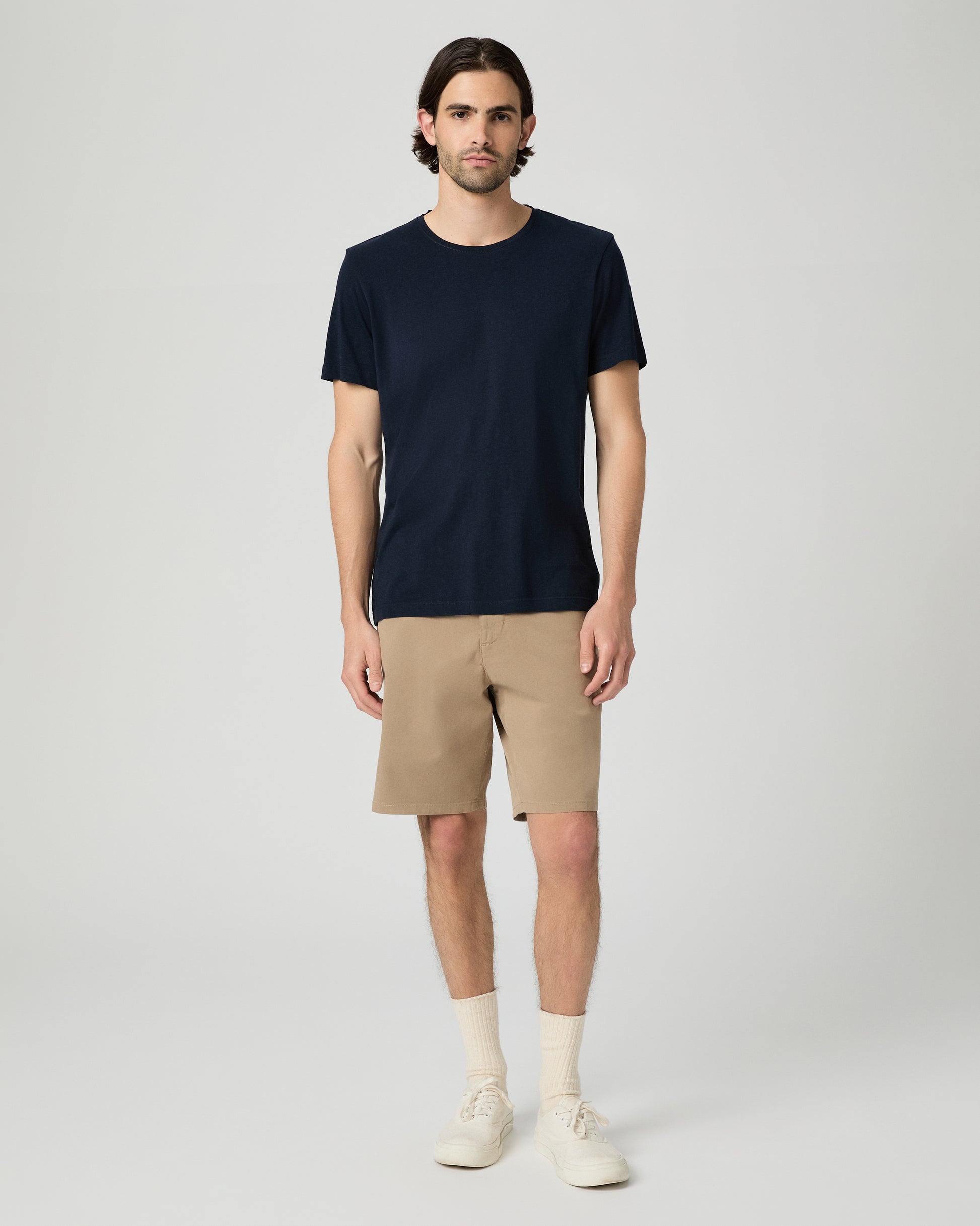 Man wearing a navy t-shirt and beige shorts on a white background