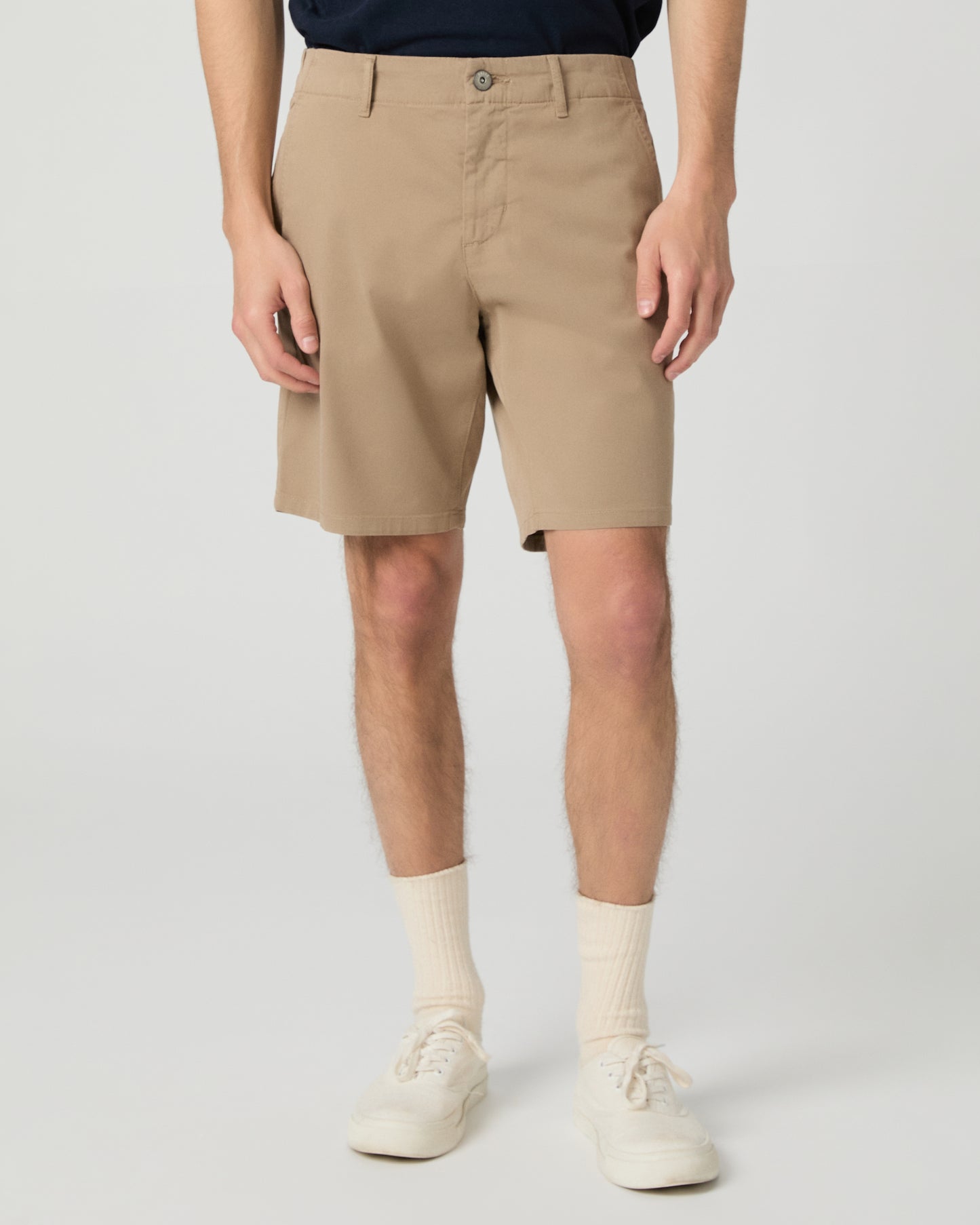 Man wearing a navy t-shirt and beige shorts on a white background