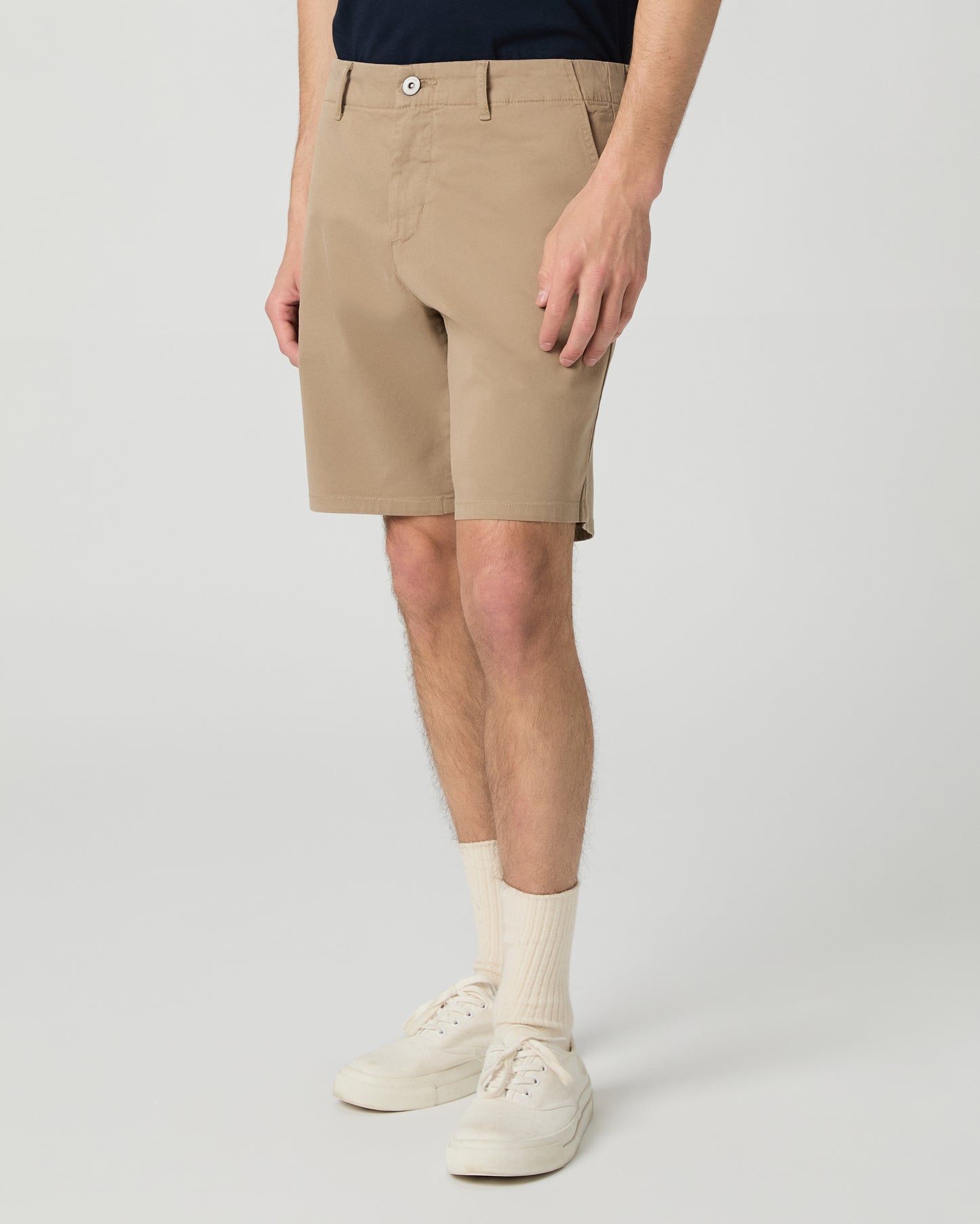 Man wearing a navy t-shirt and beige shorts on a white background