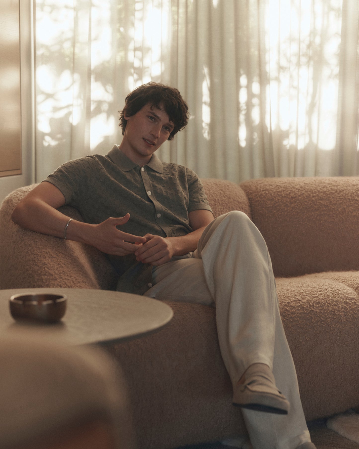Person sitting on a couch in a softly lit room with curtains.