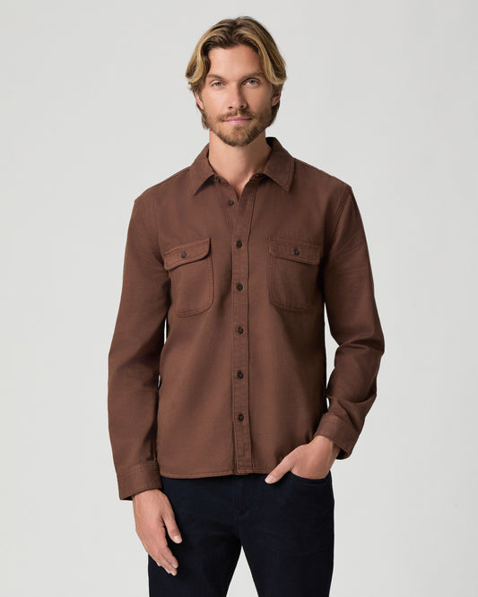 Model standing with one hand in his pocket, wearing the Martin Shirt in Vintage Sepia Clay, a brown button-front shirt with two chest pockets, with dark jeans