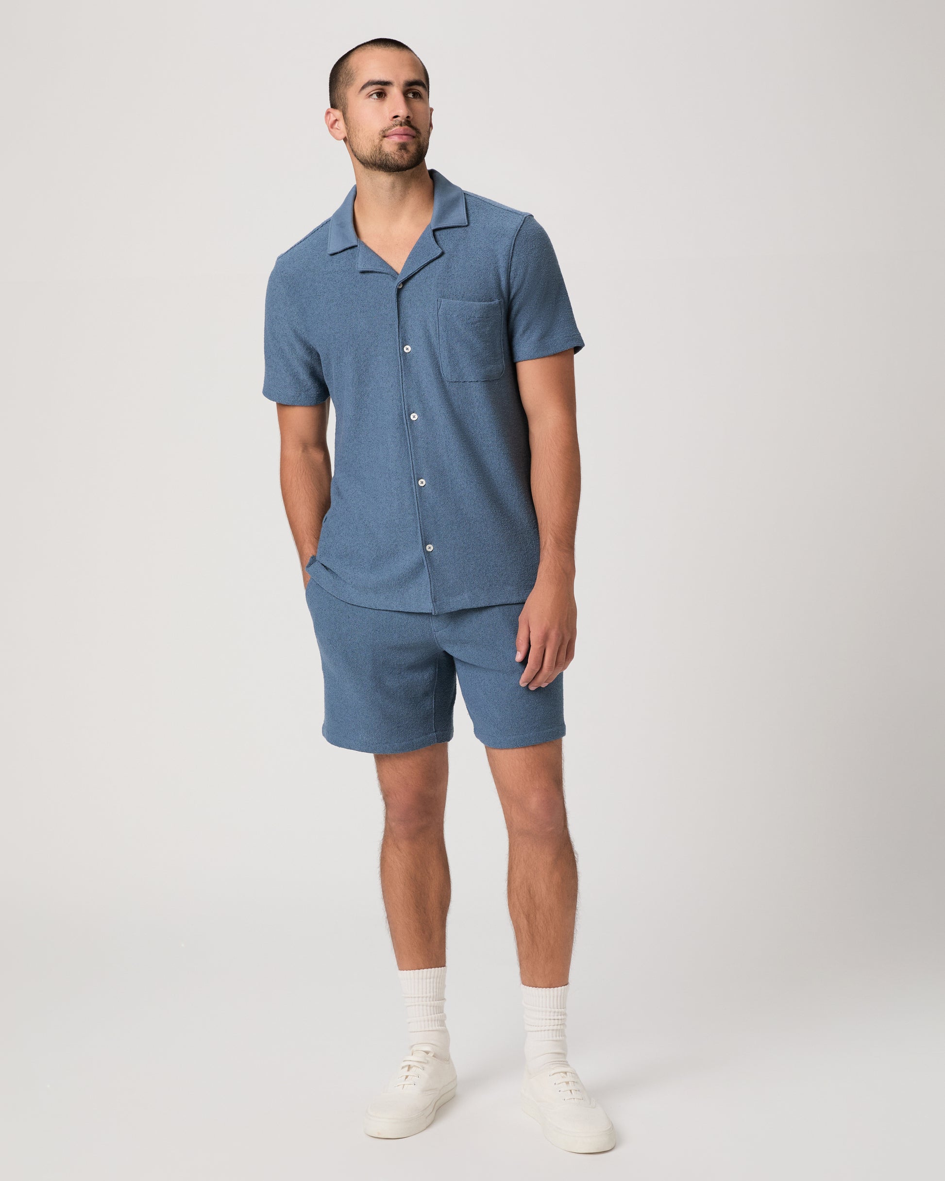 Man wearing a blue short-sleeve shirt and shorts on a light gray background