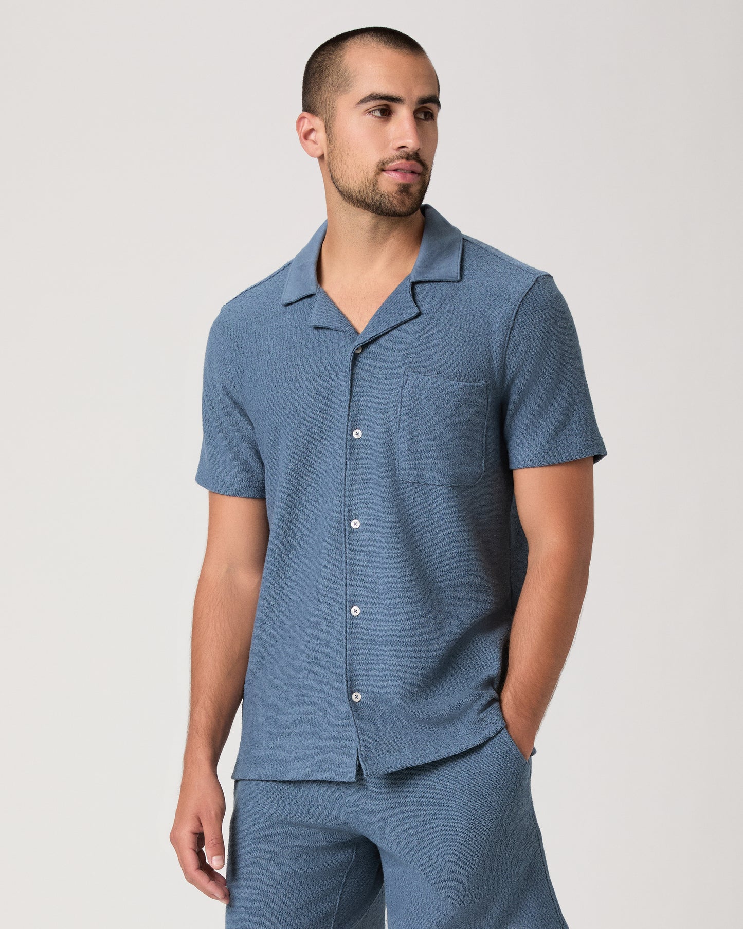 Man wearing a blue short-sleeve shirt and shorts on a light gray background