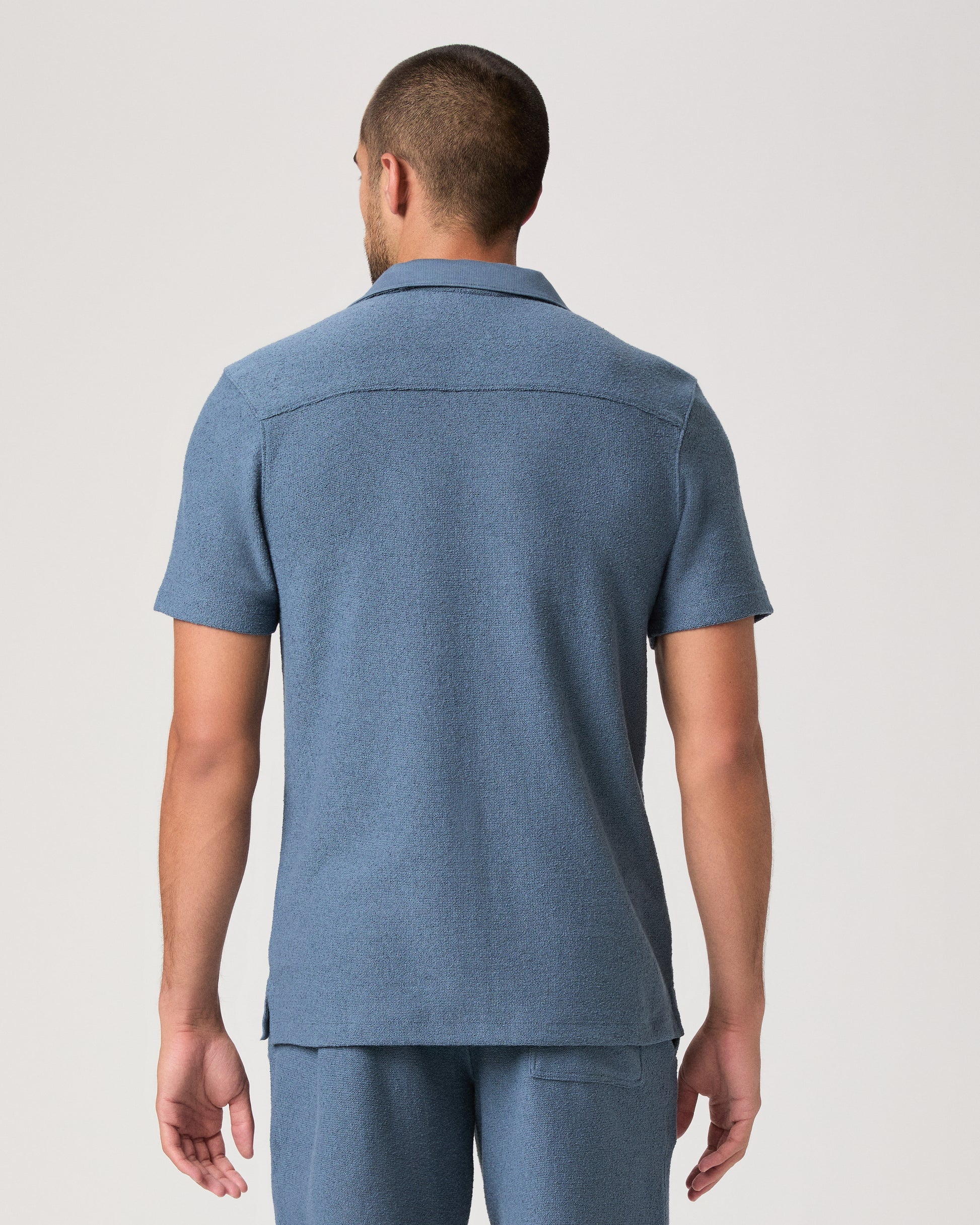 Man wearing a blue short-sleeve shirt and shorts on a light gray background