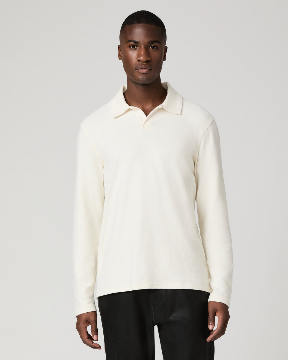 Front torso view of a man wearing a natural off-white long-sleeve polo shirt with an open ribbed-knit collar, paired with black trousers, arms relaxed at his sides.