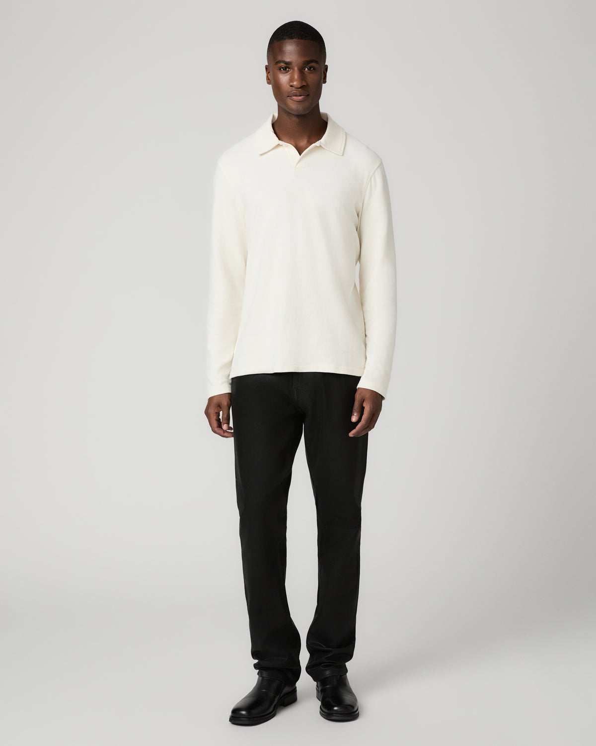 Full-length front view of a man wearing the natural off-white long-sleeve polo shirt tucked with black trousers and black leather shoes, standing straight with arms at his sides.