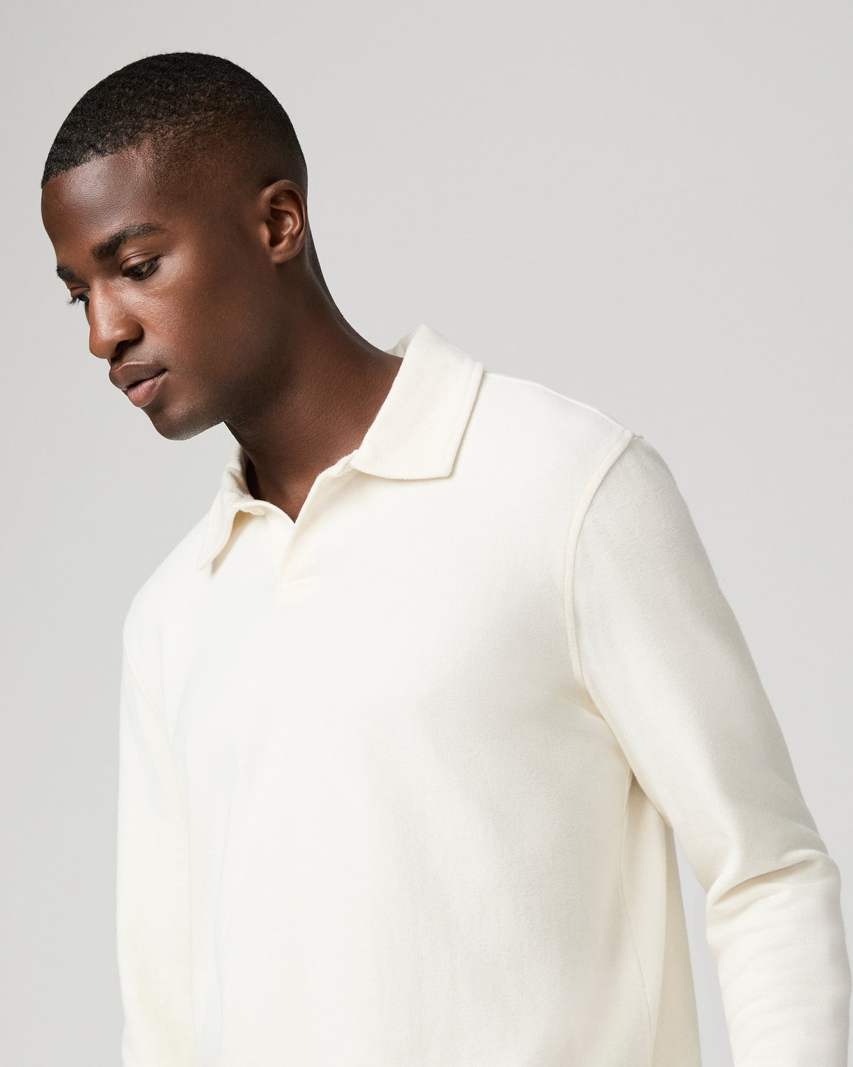 Close-up front view of a man wearing the natural off-white polo shirt, looking down and to the side, showing the open collar and placket detail at his chest.
