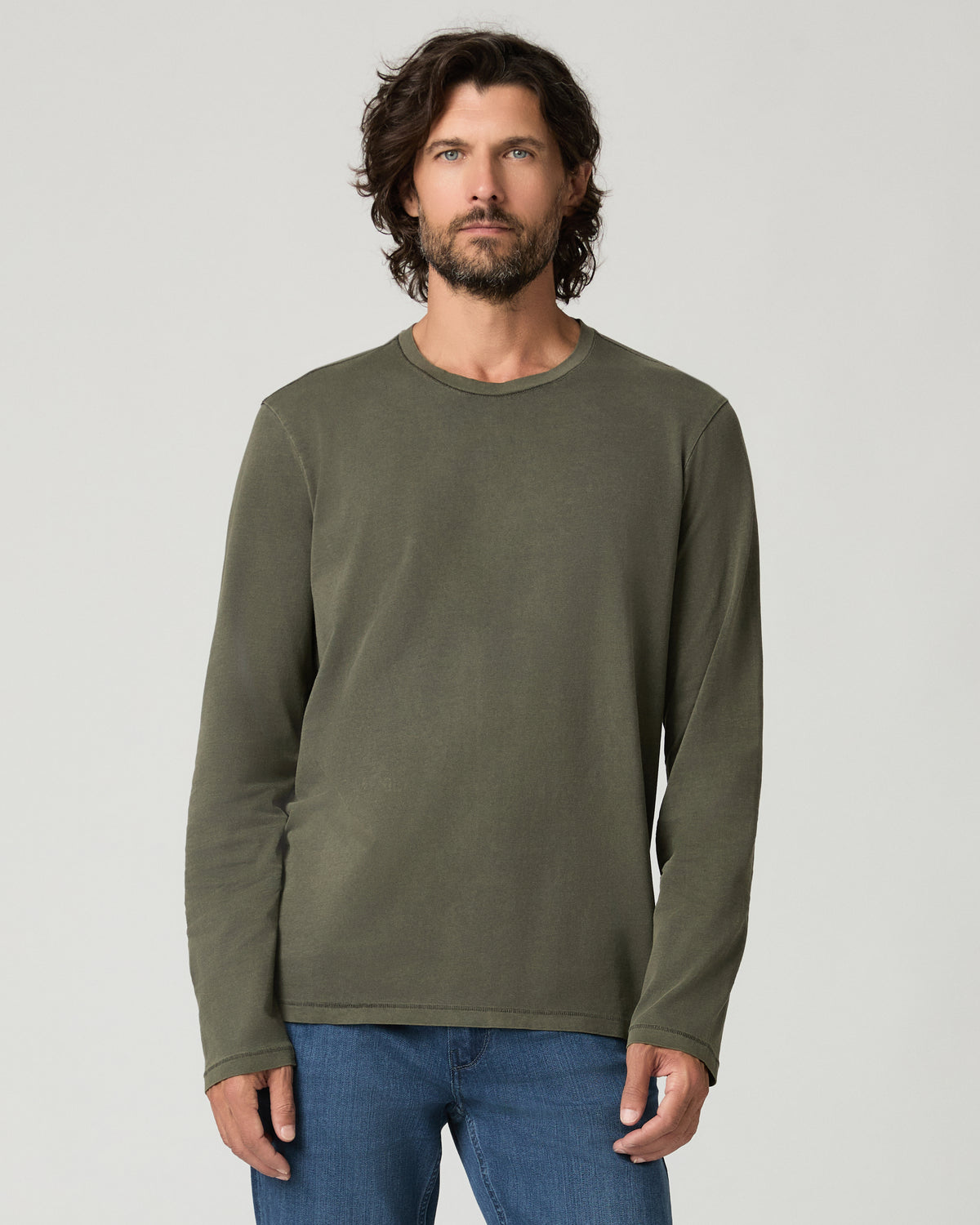 Cropped front view of a man with curly hair wearing a vintage fatigue green long-sleeve crewneck shirt with a raw-edge neckline, paired with blue denim jeans.