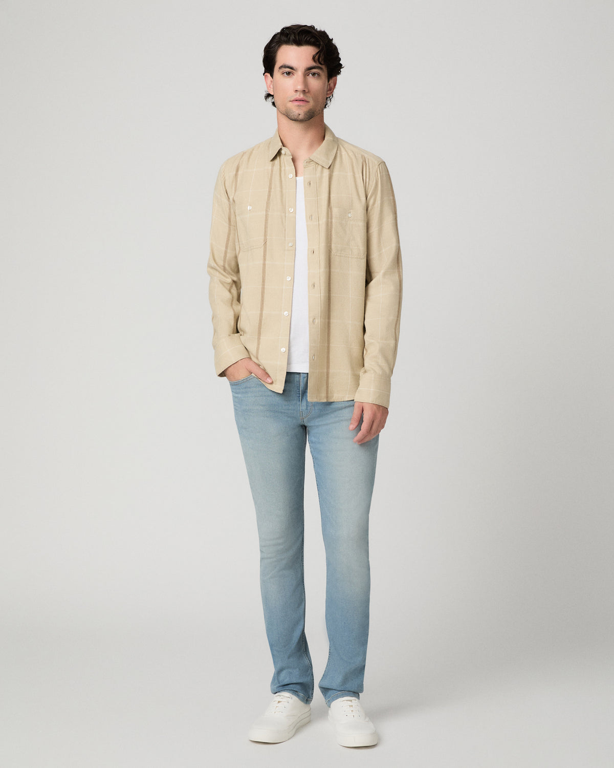 Man wearing beige shirt with light blue jeans against a white background