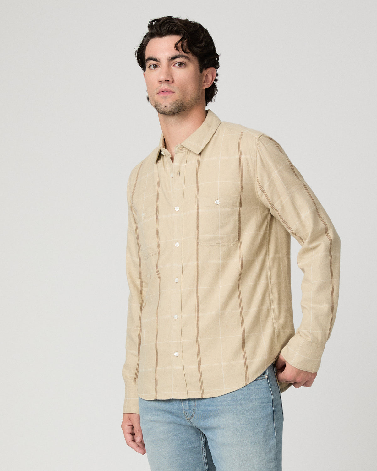 Man wearing beige shirt with light blue jeans against a white background