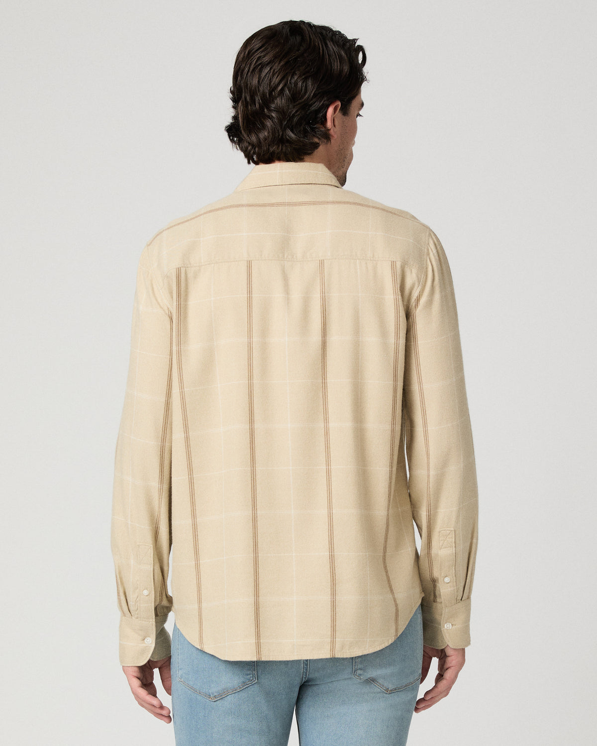 Man wearing beige shirt with light blue jeans against a white background