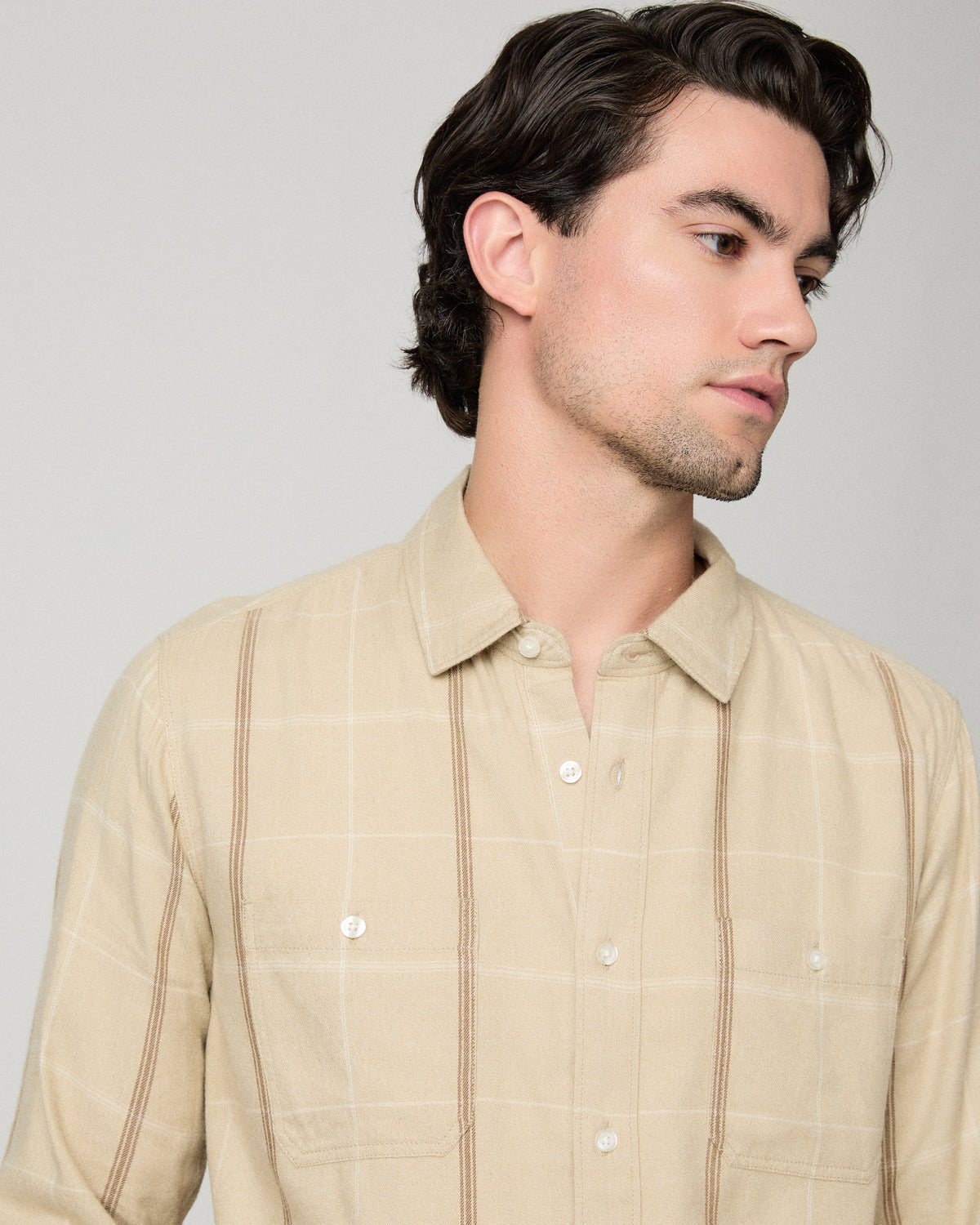 Man wearing beige shirt with light blue jeans against a white background