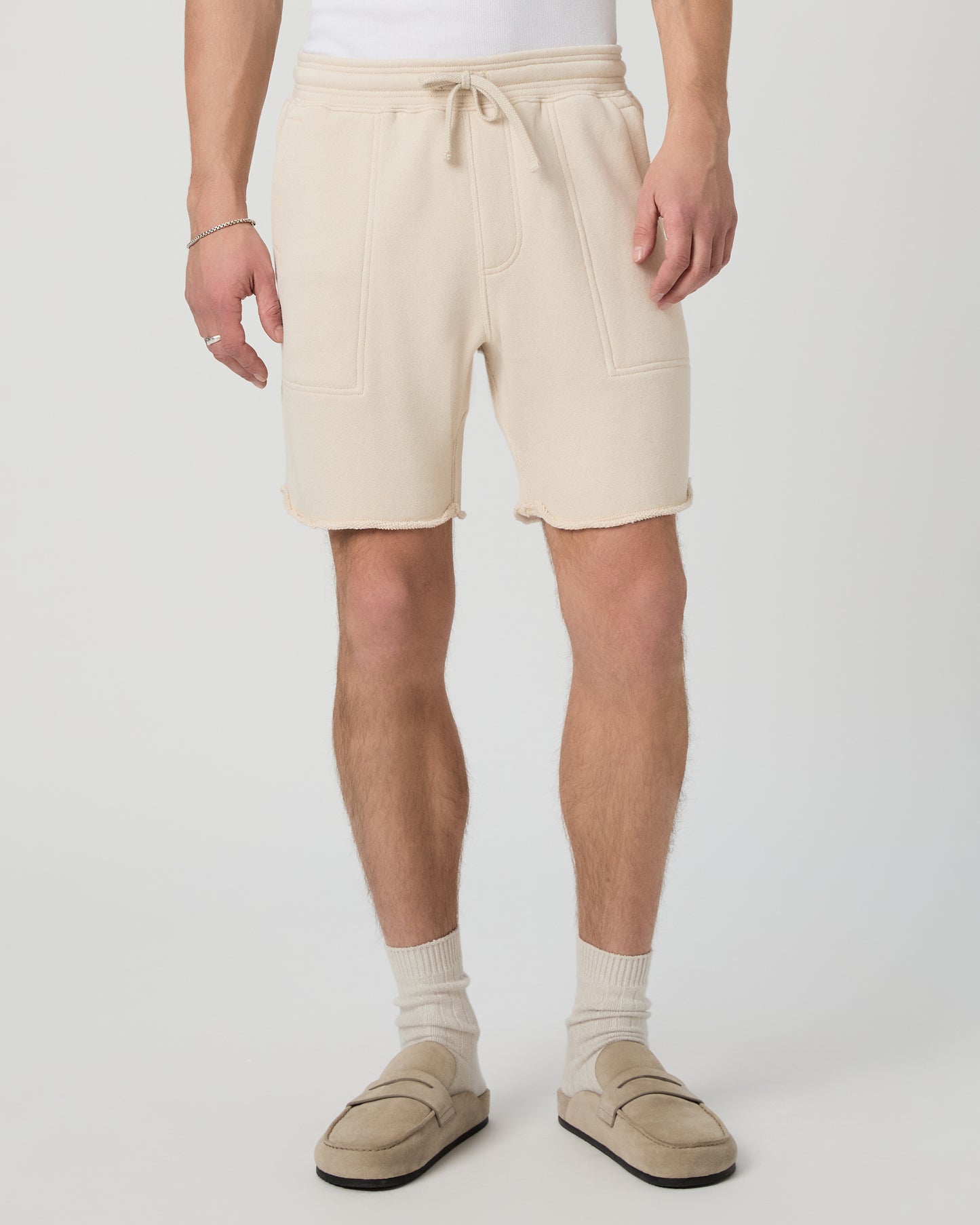 Man wearing a white shirt, beige shorts, and shoes on a plain background