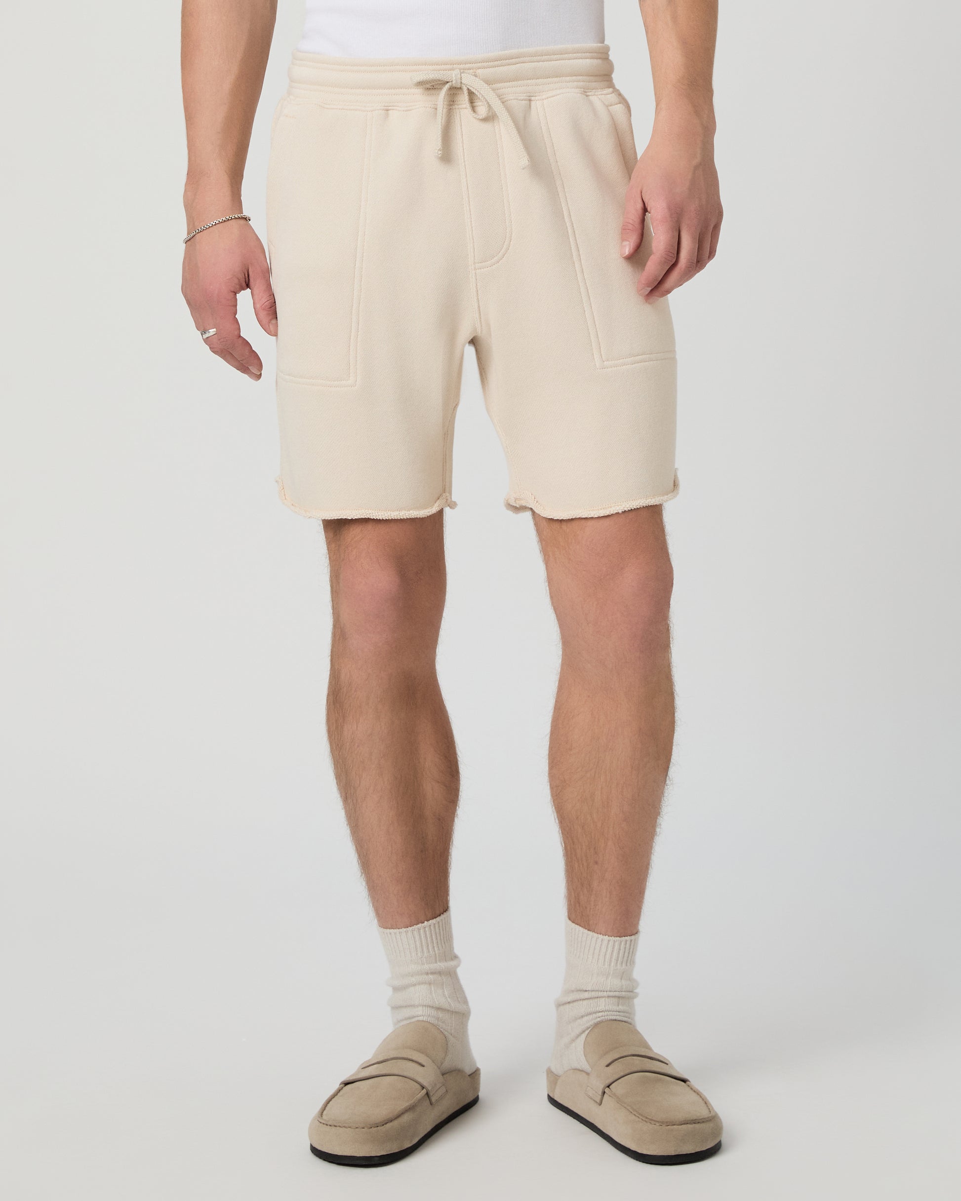 Man wearing a white shirt, beige shorts, and shoes on a plain background