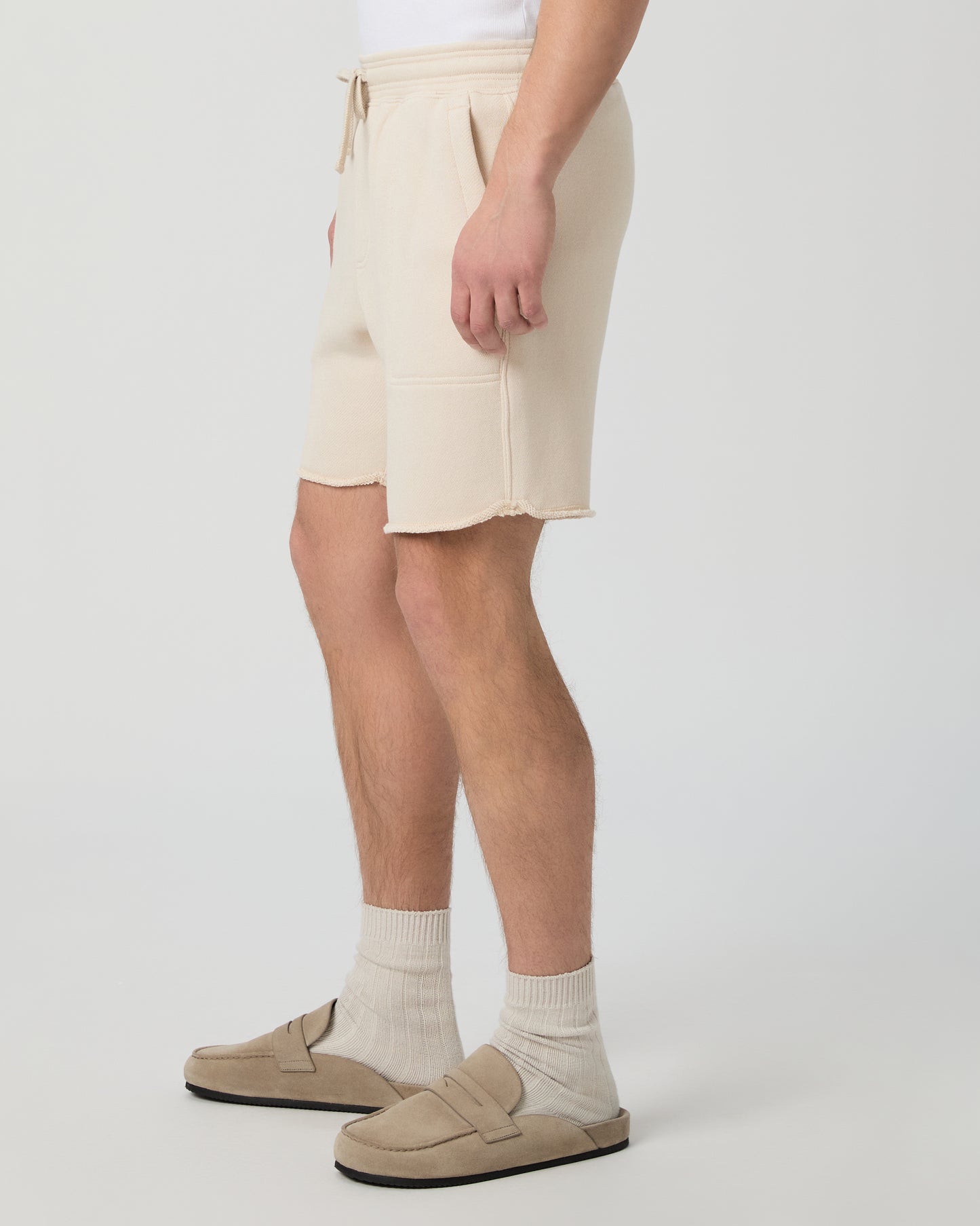 Man wearing a white shirt, beige shorts, and shoes on a plain background
