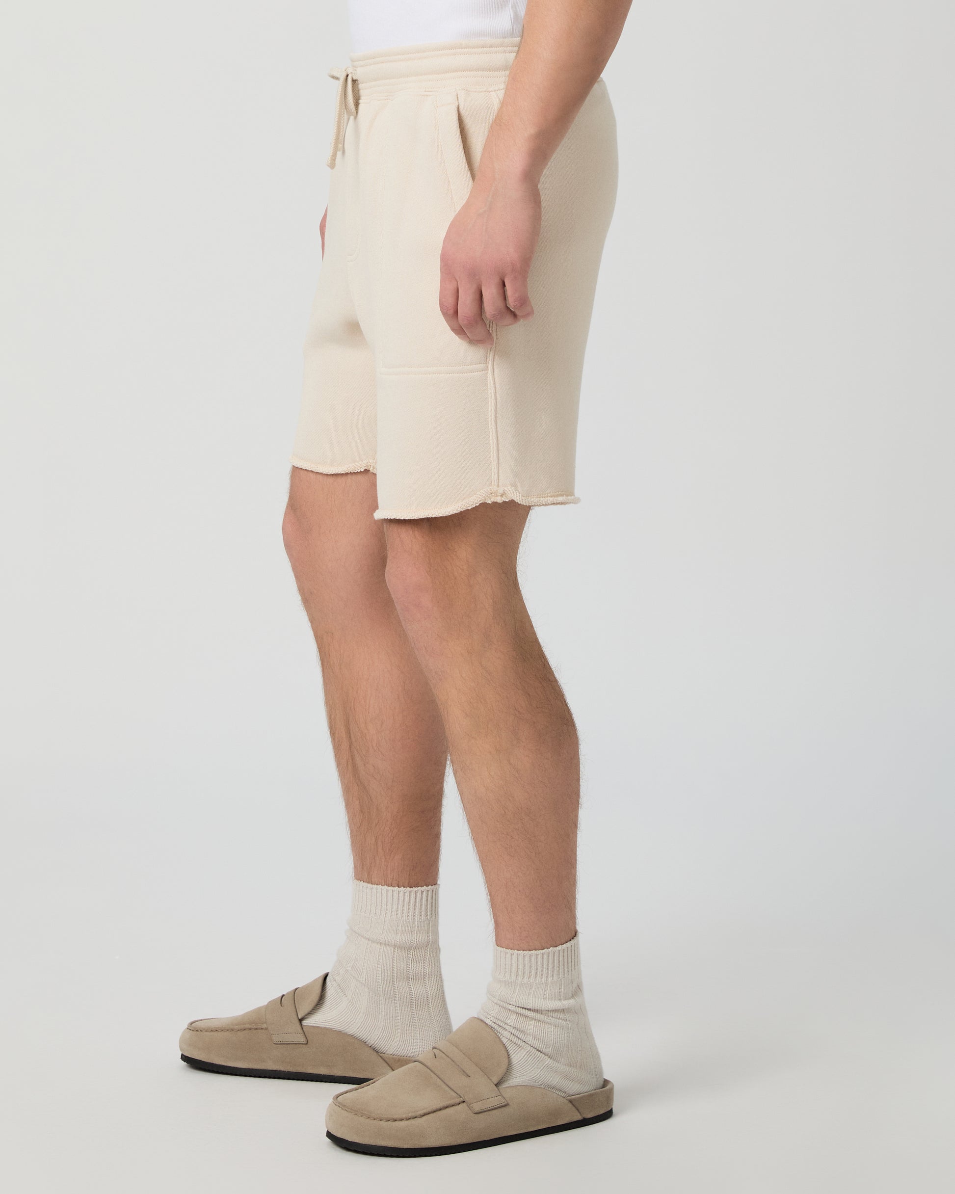Man wearing a white shirt, beige shorts, and shoes on a plain background