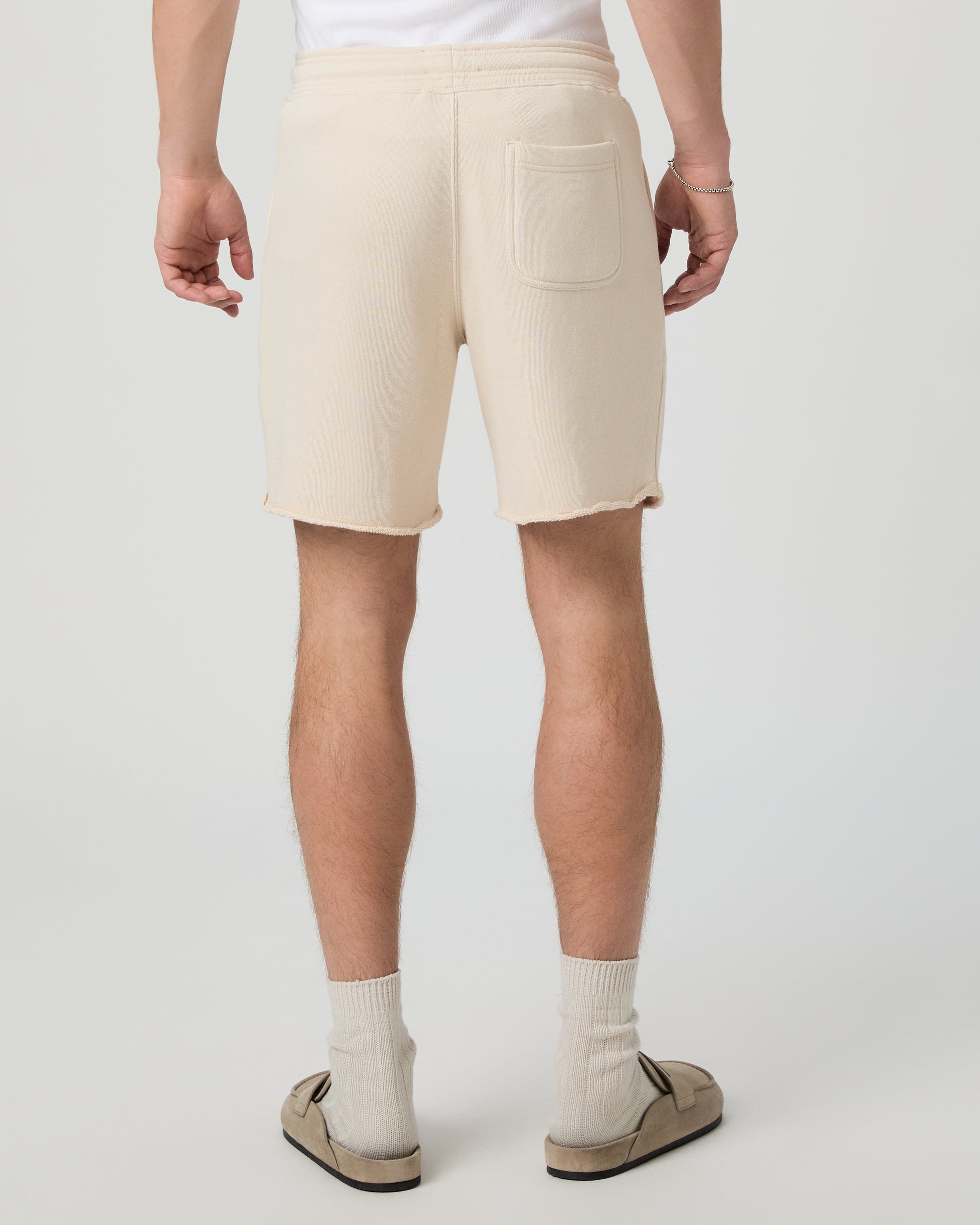 Man wearing a white shirt, beige shorts, and shoes on a plain background