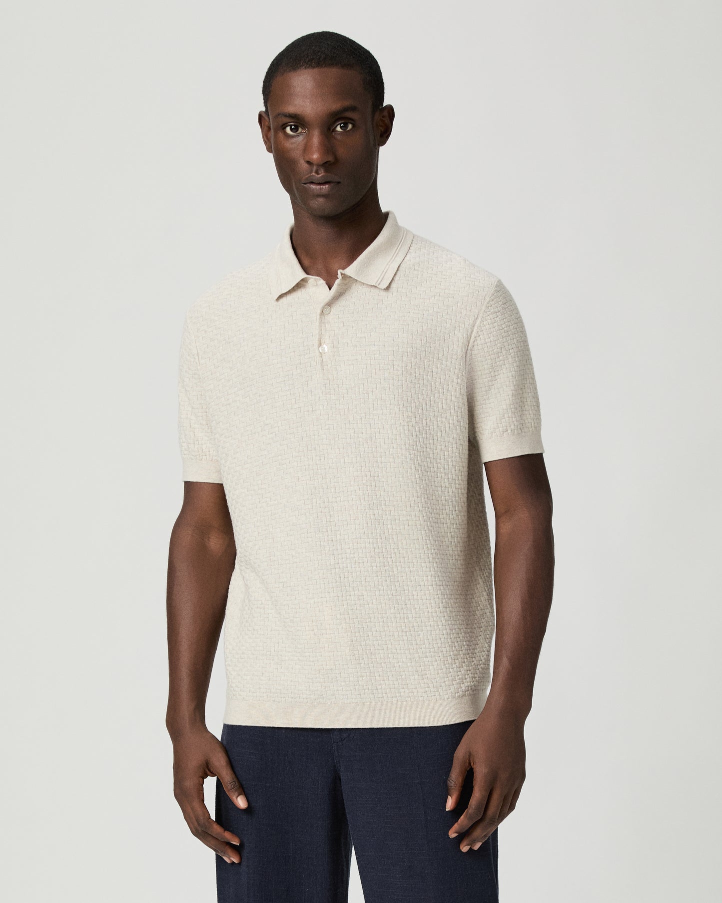 Man wearing a textured beige polo shirt with blue pants against a plain background